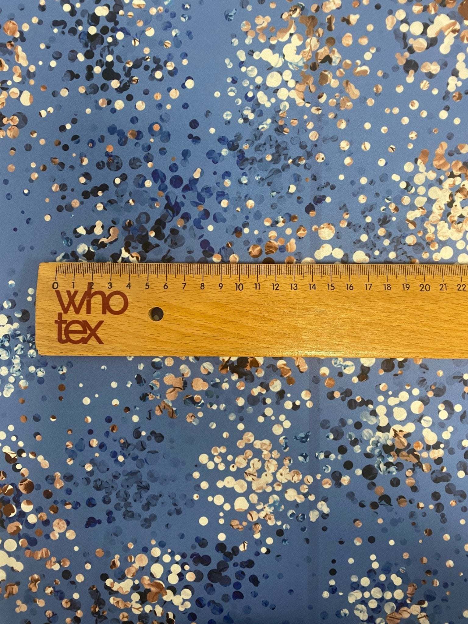multicolor confetti pattern abstract dot print on blue fabric with wooden ruler showing scale