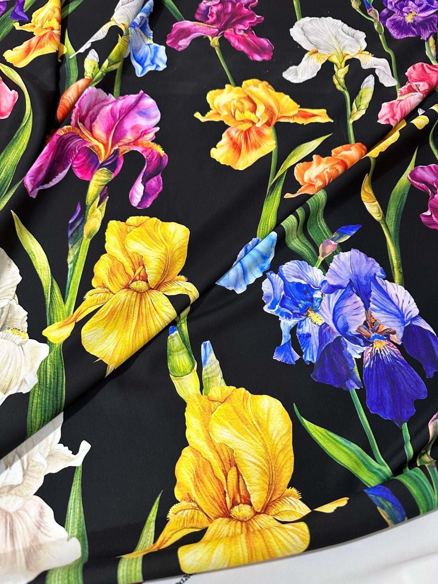 Black floral crepe fabric with vibrant yellow, purple, pink, white, and blue flowers and green leaves