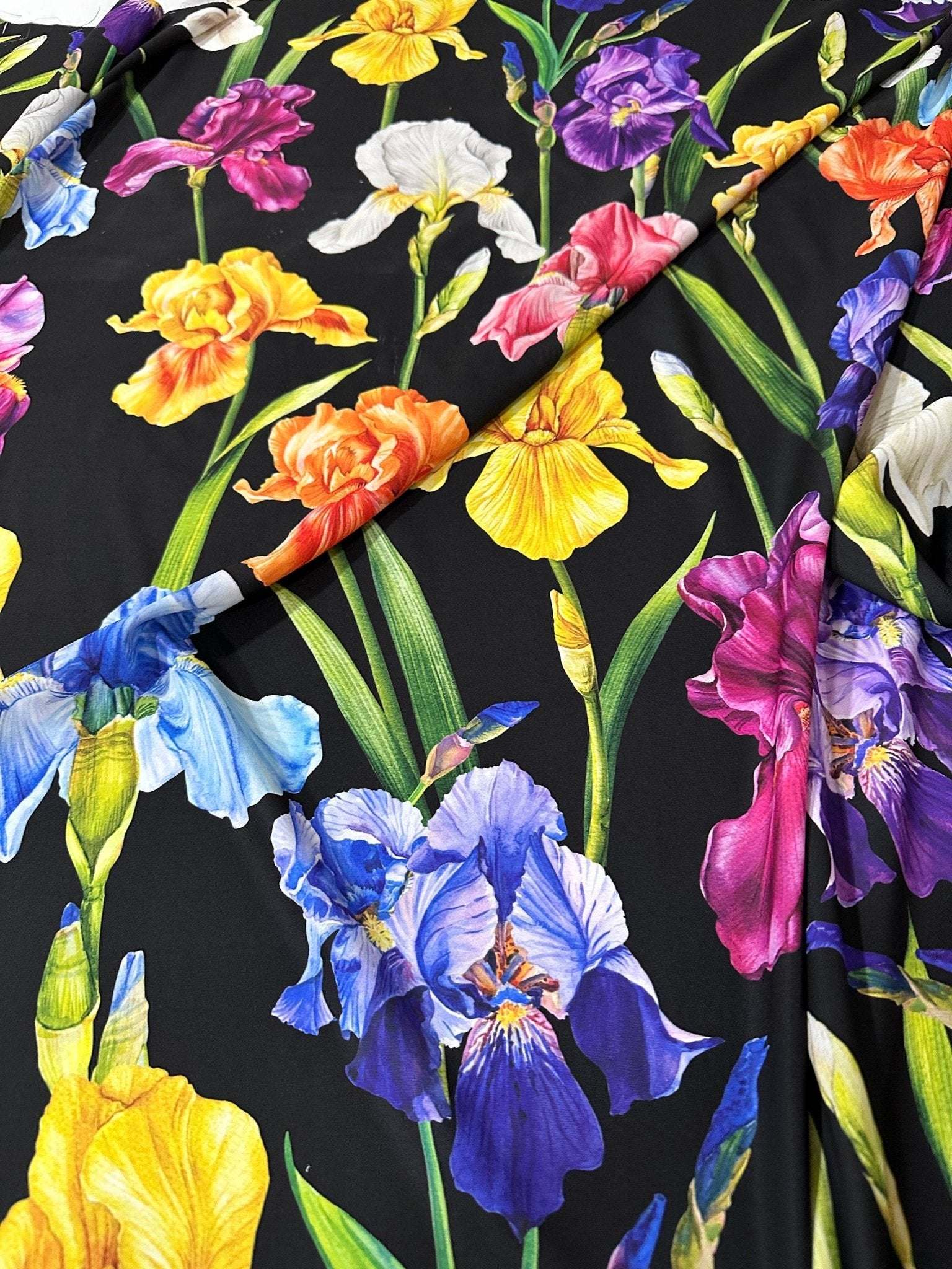 Black floral crepe fabric with colorful iris flower pattern, lightweight and soft textured material ideal for dresses and blouses