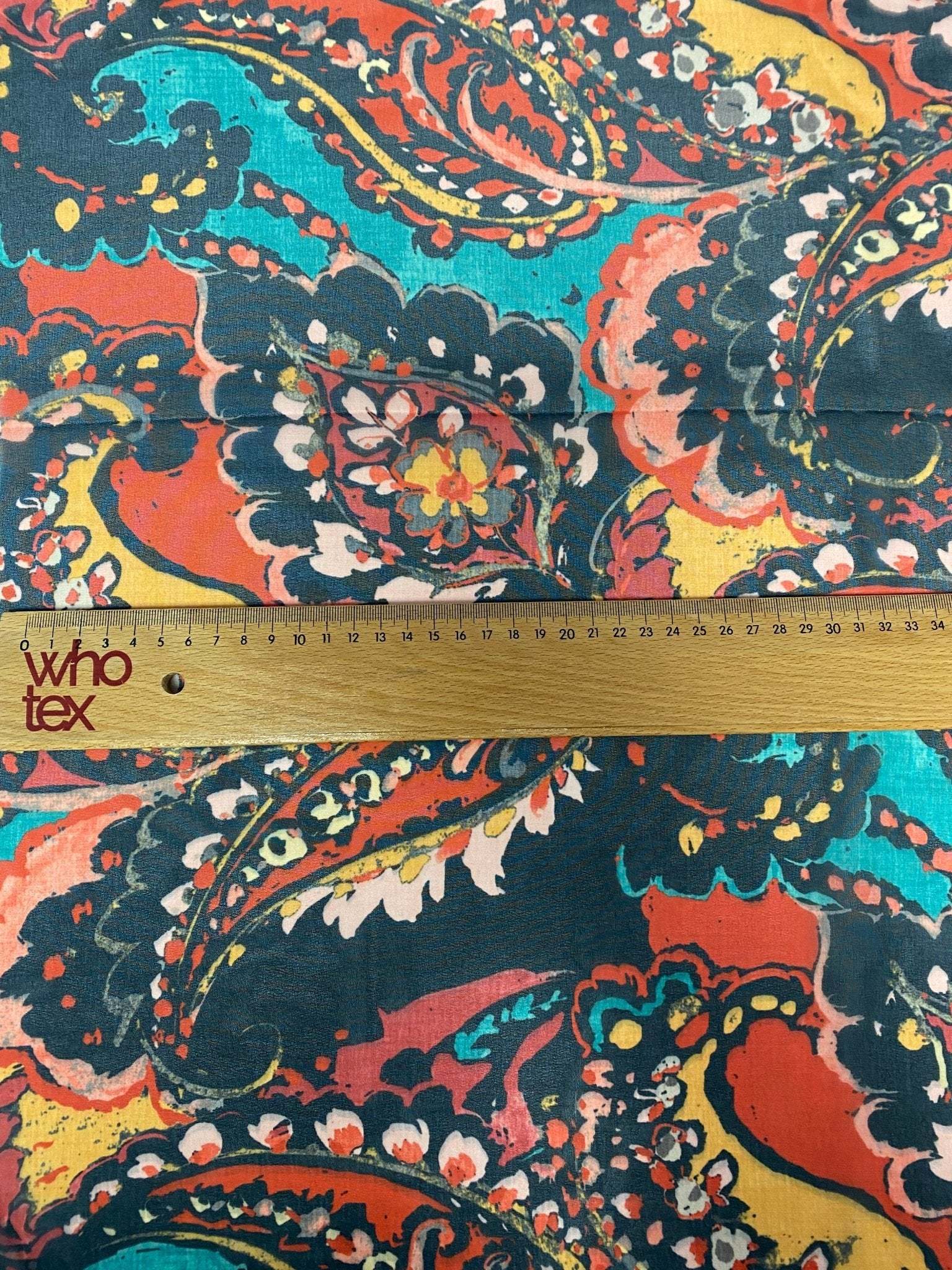 close-up of vibrant multicolor paisley print fabric with ruler showing scale