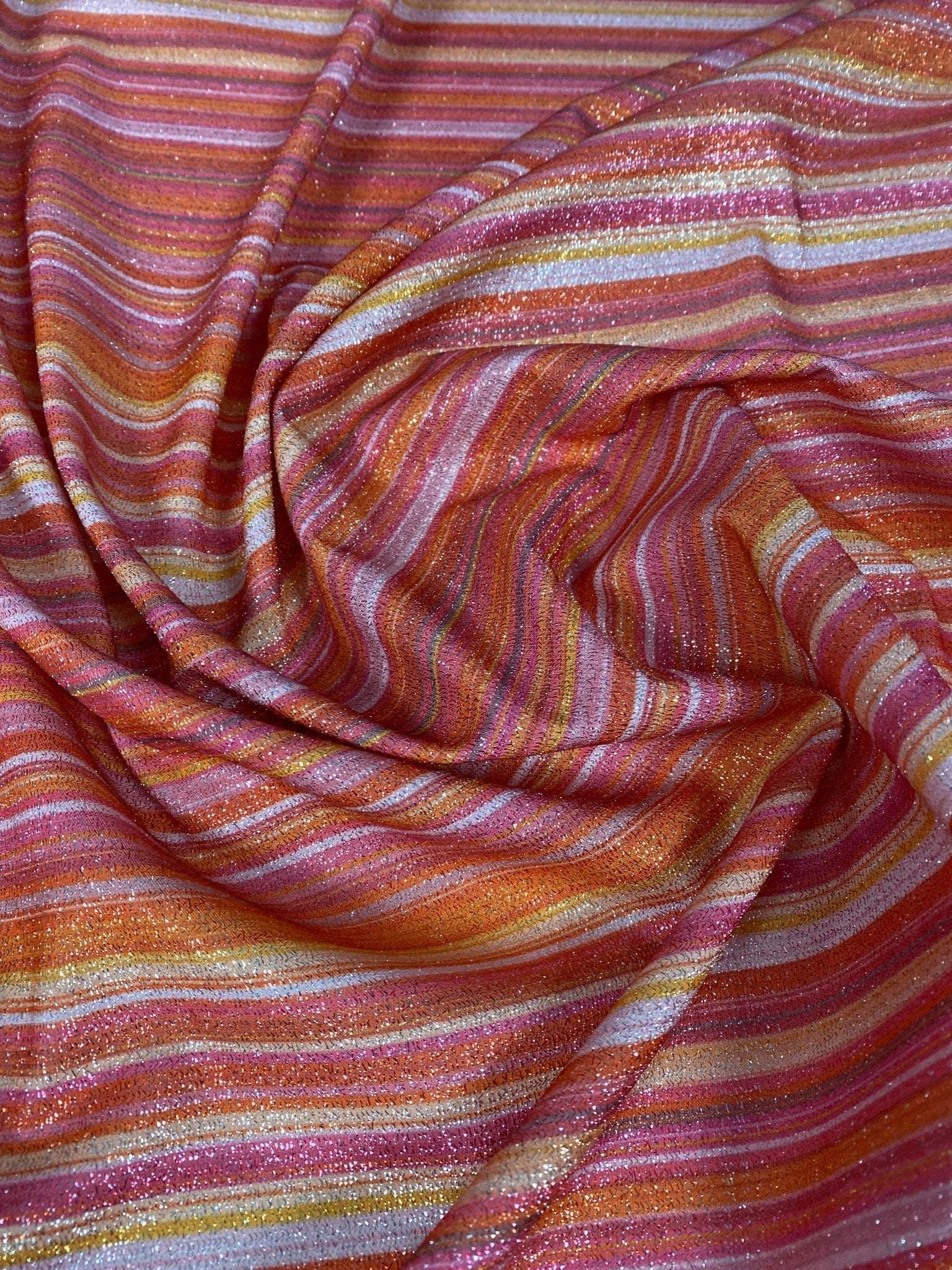 Multicolor striped glitter fabric in red, orange, and pink tones with gold lurex shimmer and 4-way stretch polyester blend