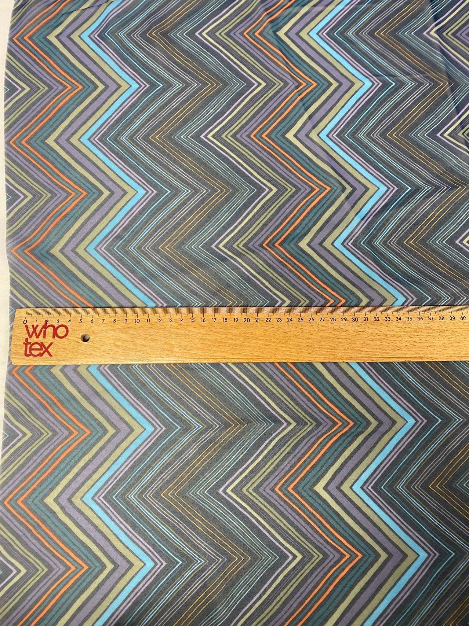 multicolor zigzag patterned fabric with ruler for scale showing vibrant chevron design in multiple colors