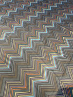 Multicolor zigzag patterned fabric with vibrant orange, blue, brown, and beige stripes on a dark background, 150cm wide.