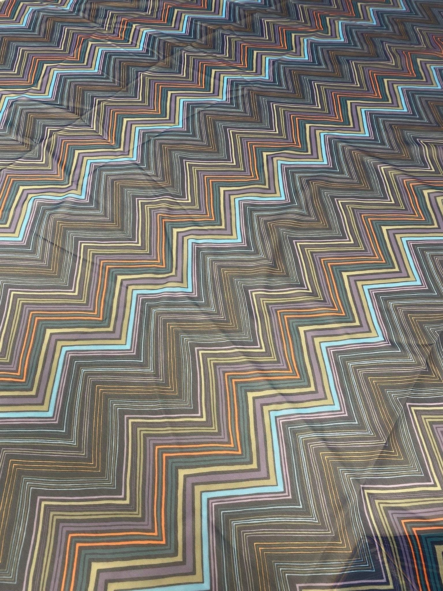 Multicolor zigzag patterned fabric with vibrant orange, blue, brown, and beige stripes on a dark background, 150cm wide.
