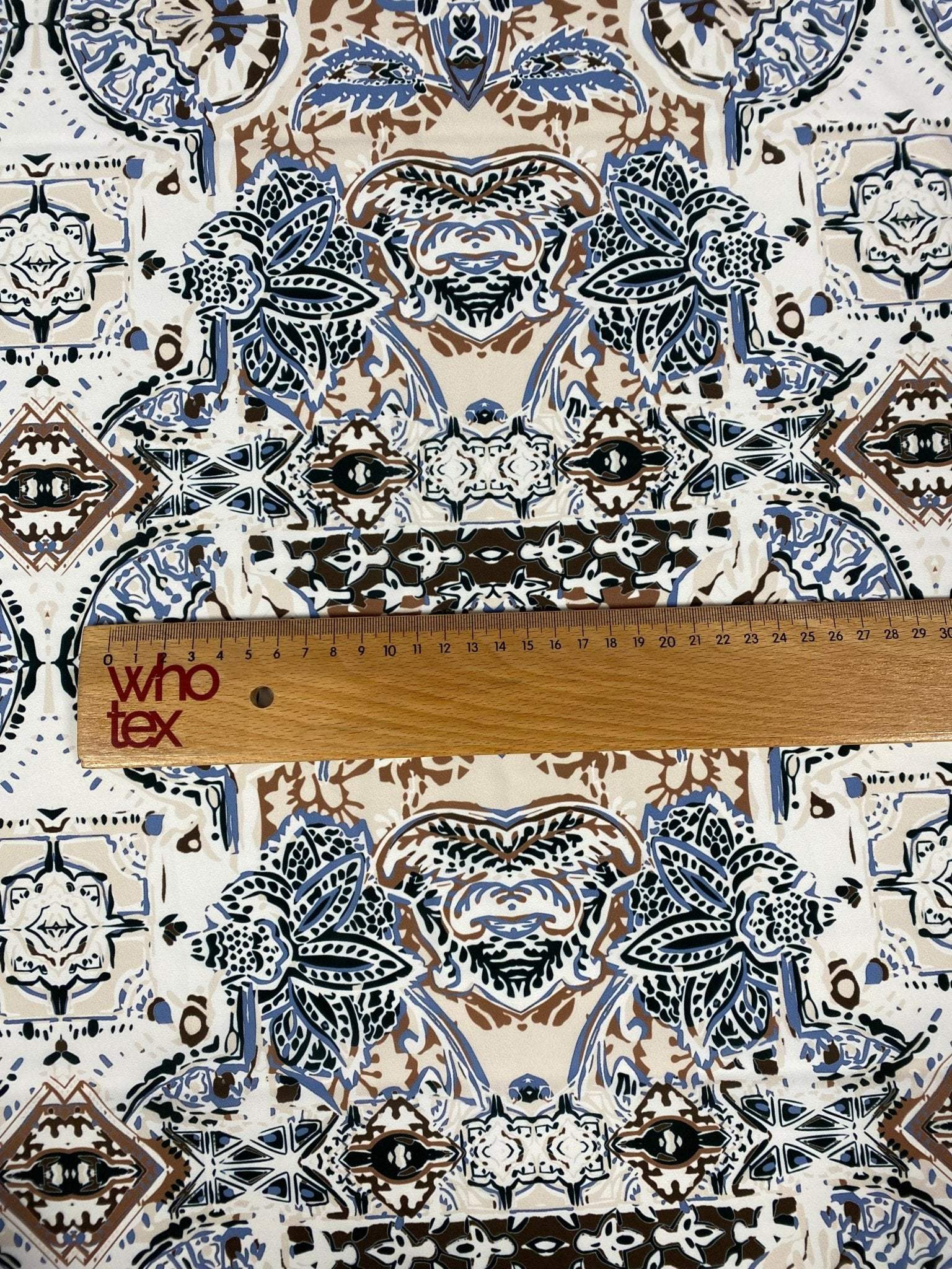 Ornamental ethnic print fabric in blue, brown, and beige with intricate patterns and ruler for scale