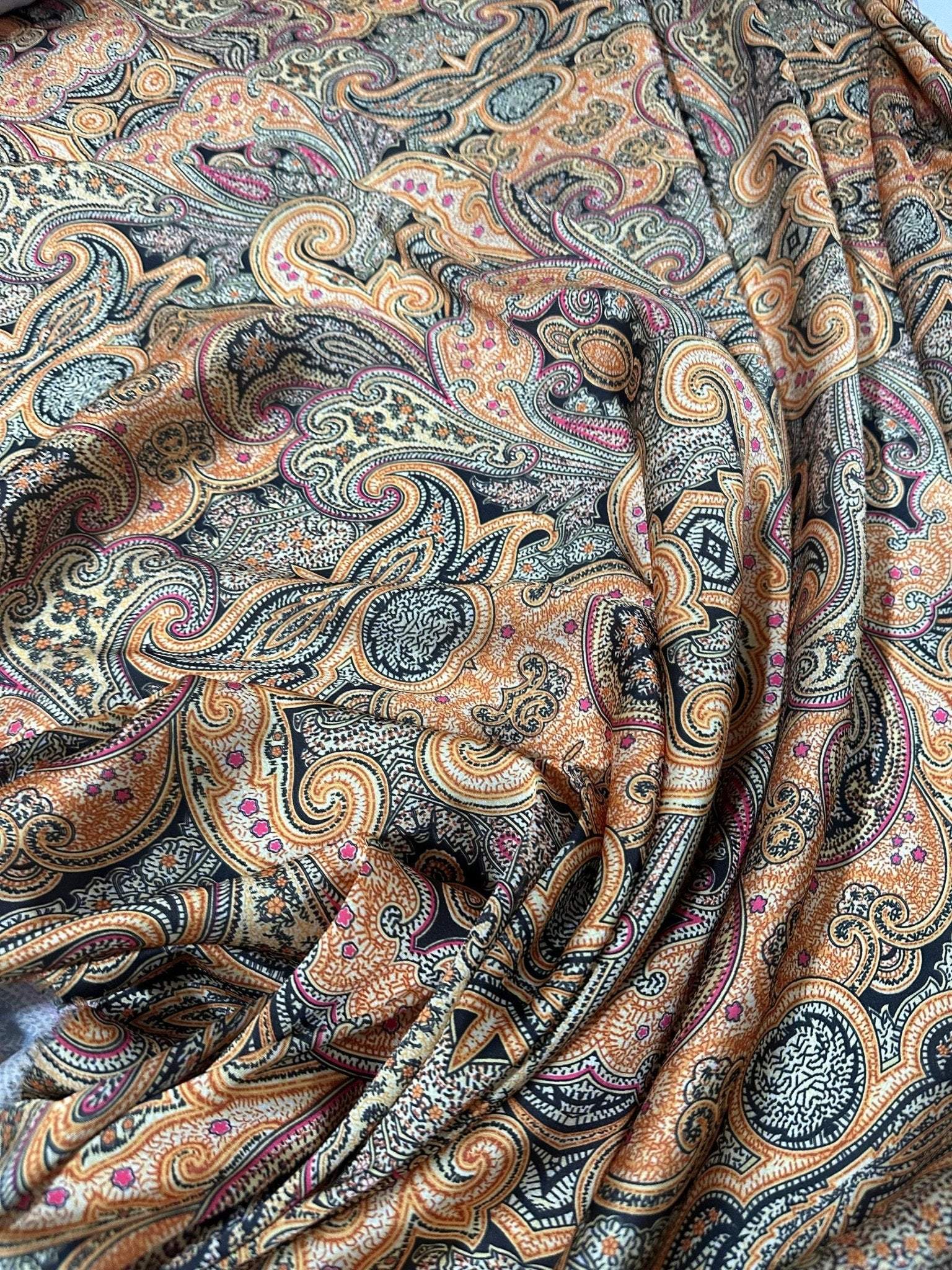 Close-up of black and orange paisley fabric with intricate swirling patterns and floral details