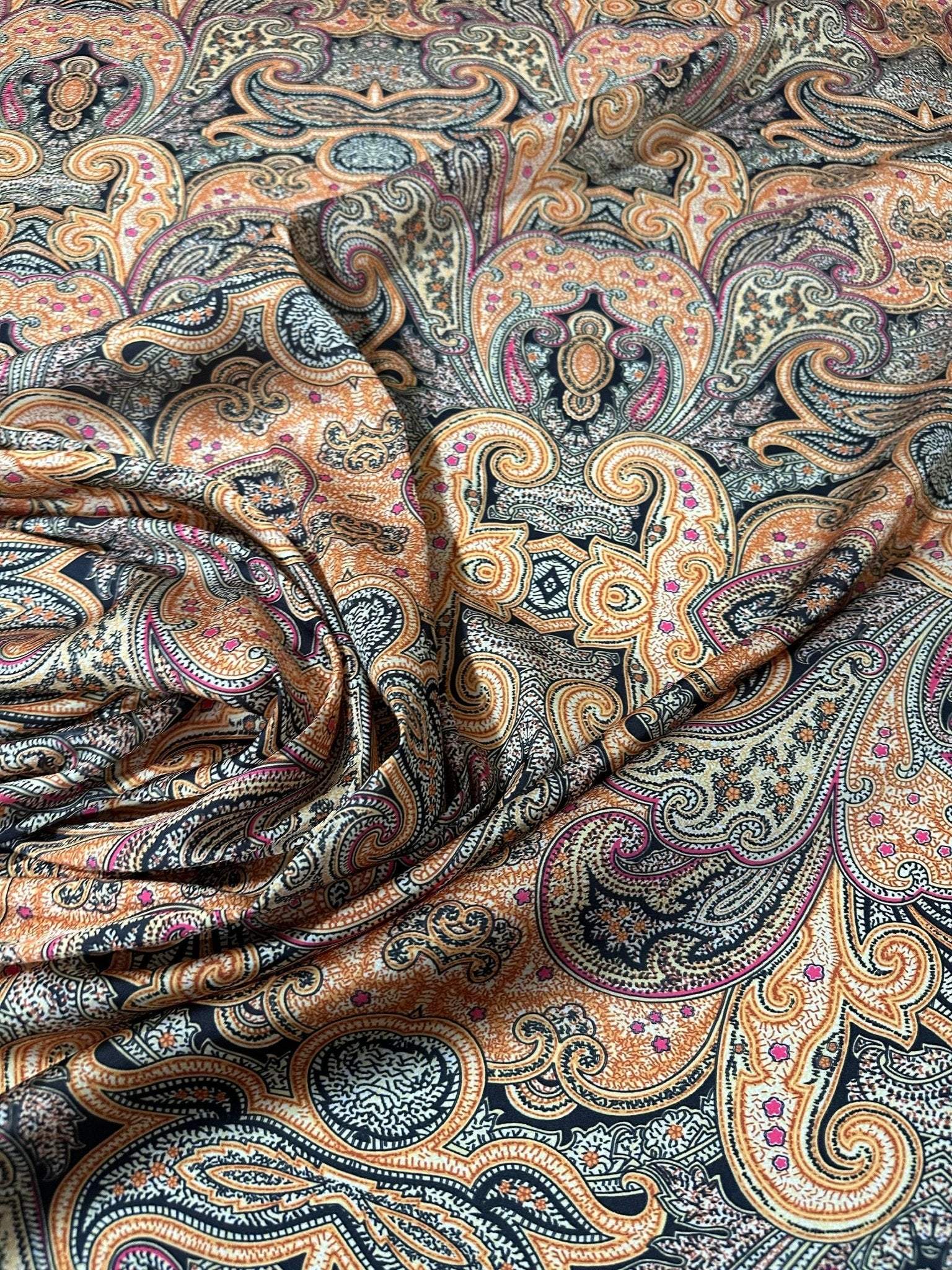 close-up of black and orange paisley fabric with intricate decorative pattern and fabric folds