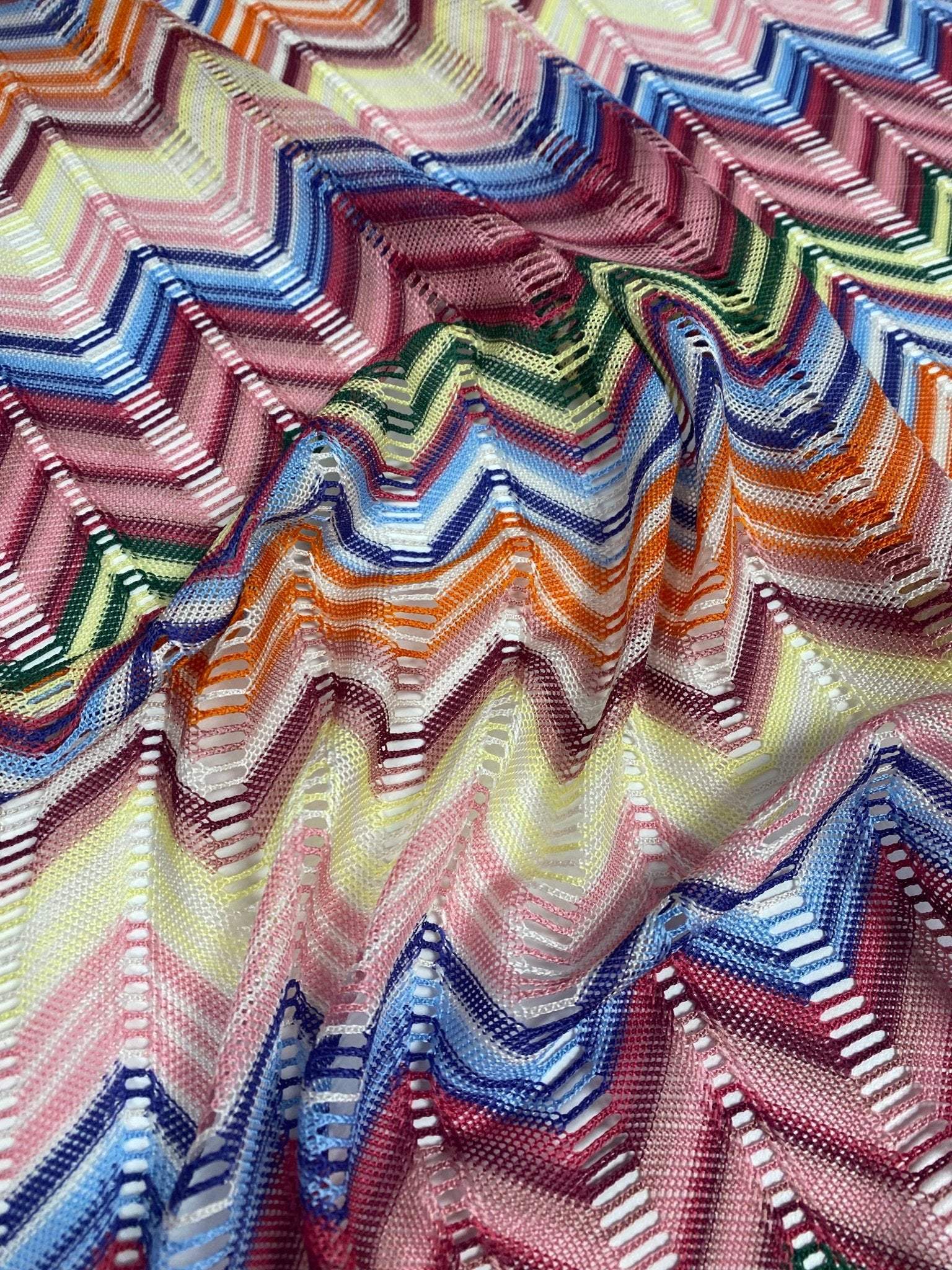 Pastel multicolor chevron mesh fabric with zigzag knit pattern in vibrant green, blue, pink, orange, and yellow tones.