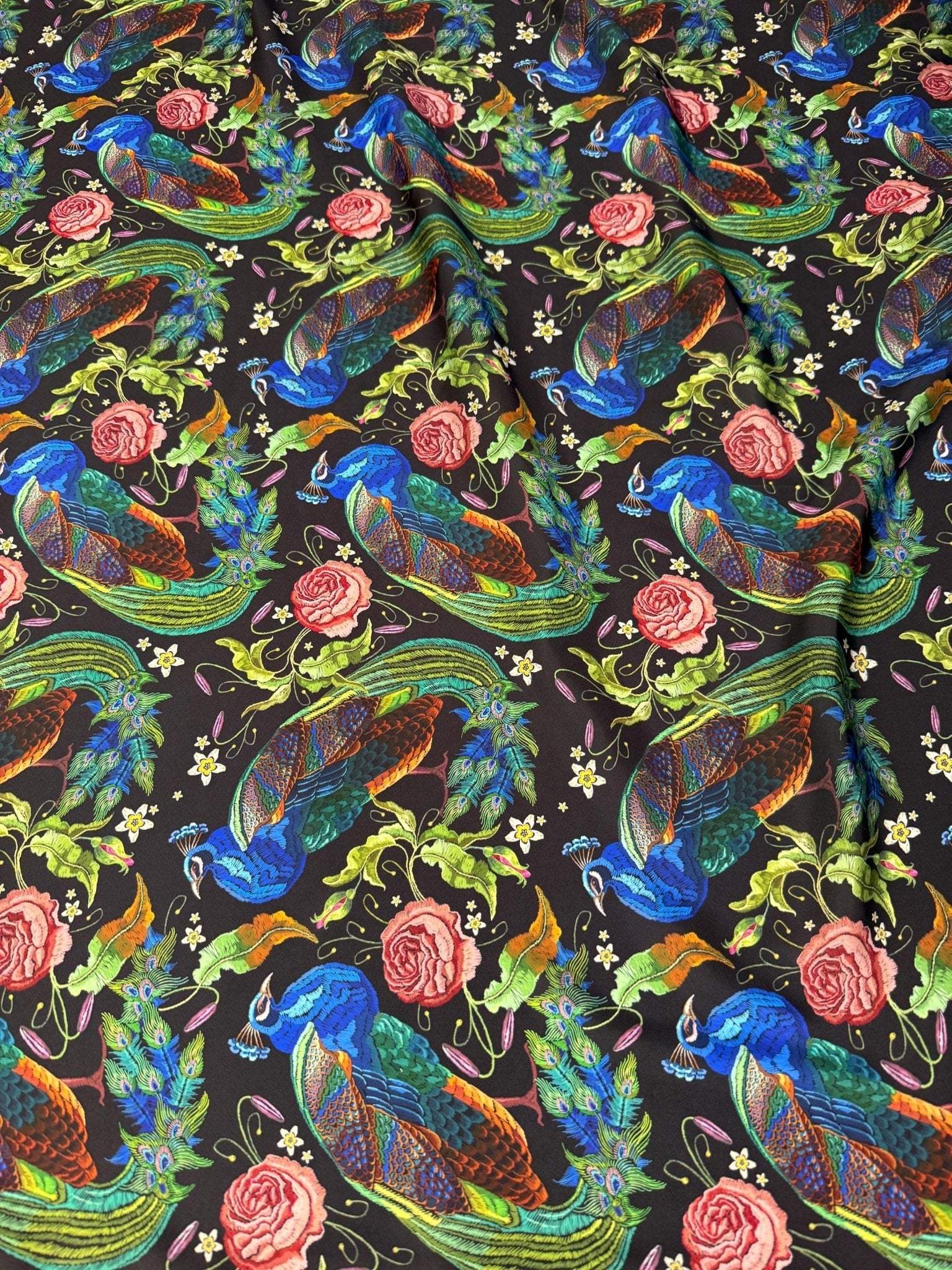 Vibrant peacock and rose patterned cotton fabric with floral and leaf motifs on dark background, ideal for sewing and quilting projects.