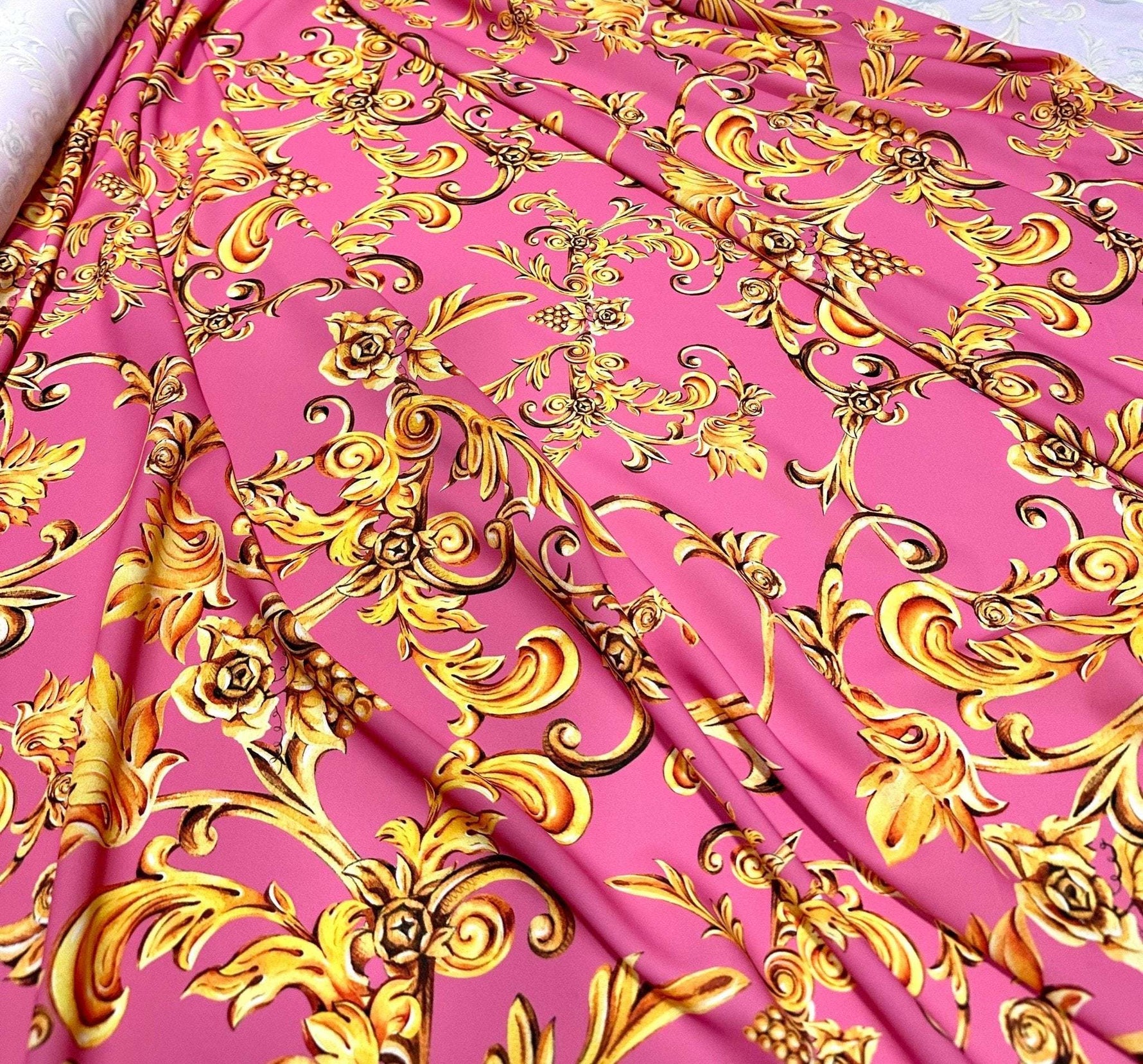 Pink and gold Baroque print fabric with ornate floral and scroll designs, ideal for upholstery and decorative projects
