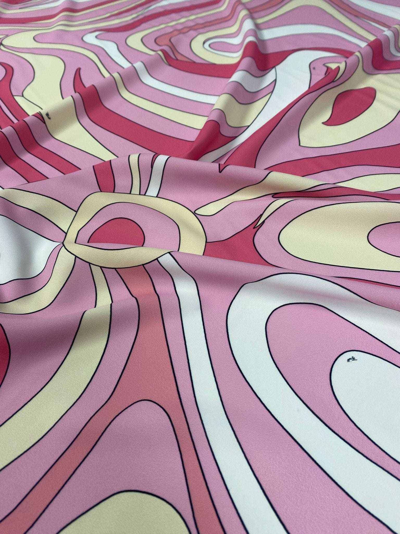 Close-up of pink and yellow psychedelic swirl print fabric with vibrant swirled patterns and smooth texture