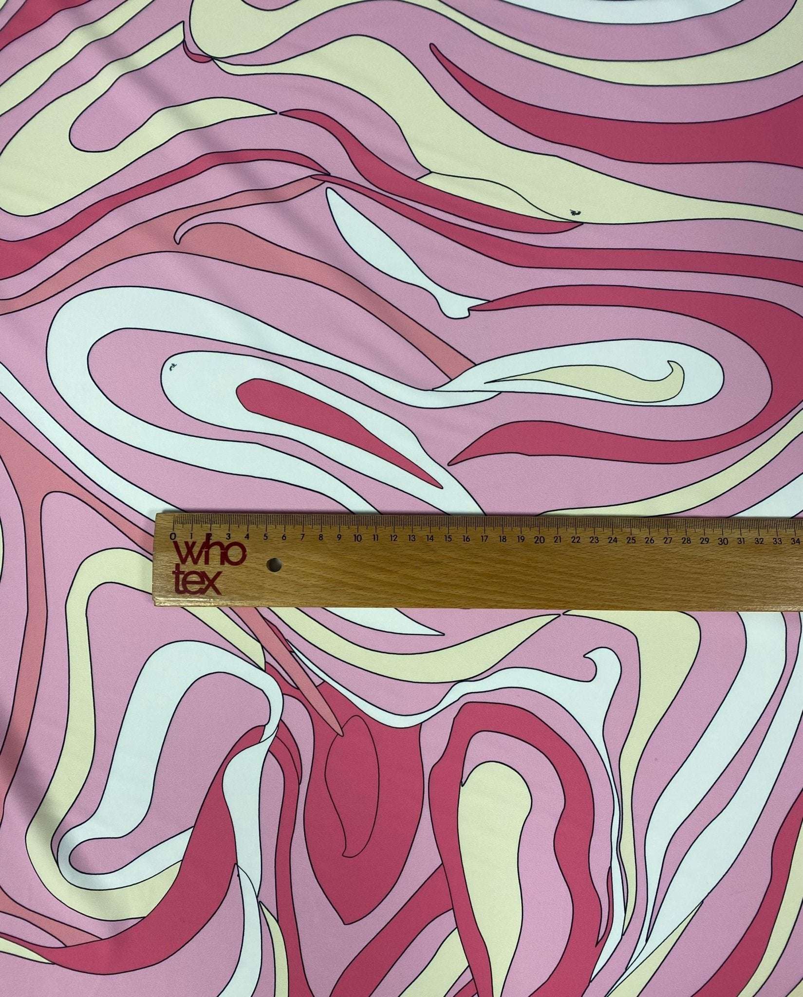 Close-up of pink and yellow psychedelic swirl print fabric with ruler for scale