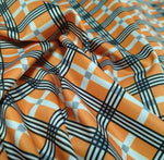 Orange, black, and white 4-way stretch plaid fabric with a smooth texture and flexible drape
