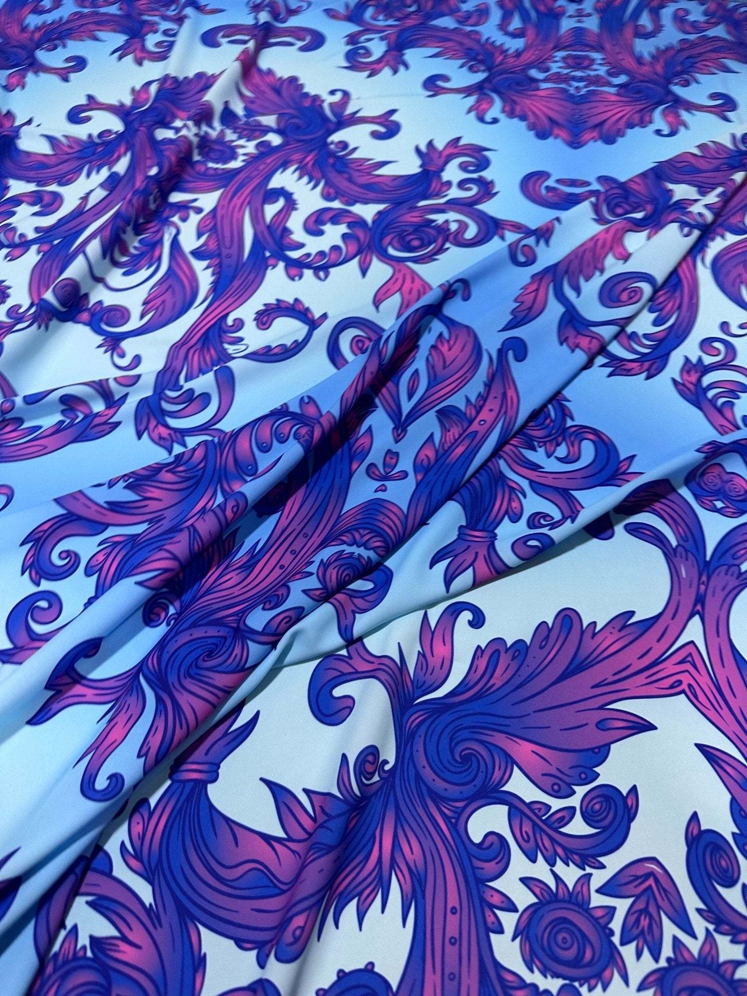 Close-up of purple and blue baroque pattern fabric with intricate swirling designs on a light blue background