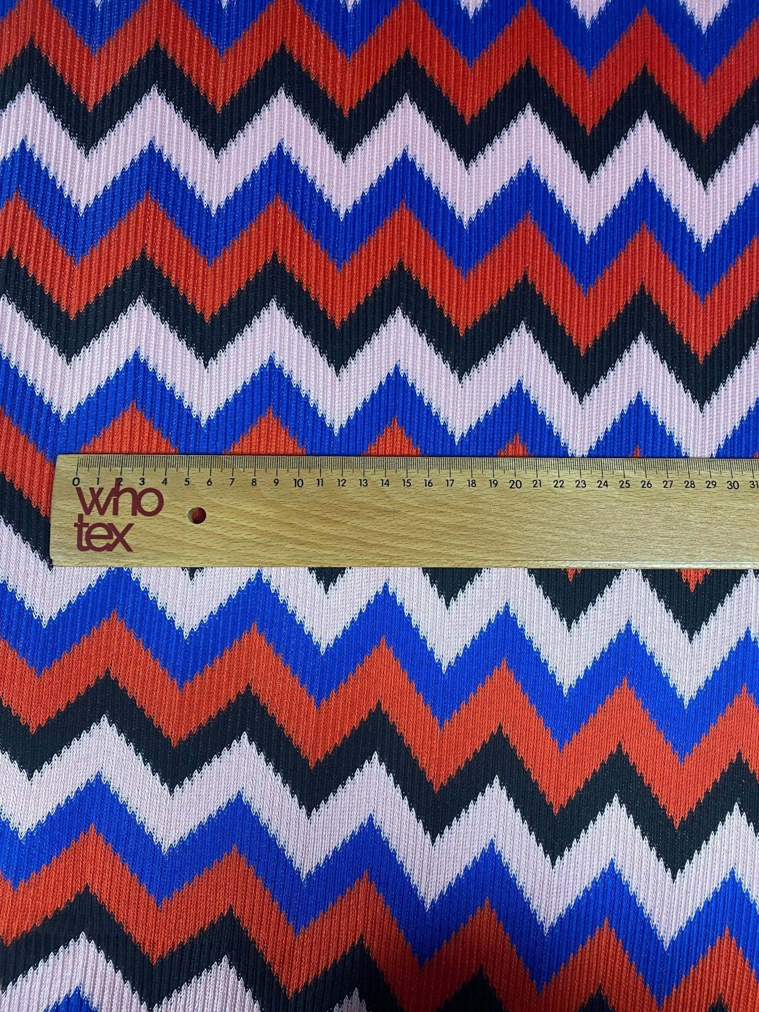 Close-up of red, blue, black zigzag chevron pattern knit fabric with measuring ruler for scale