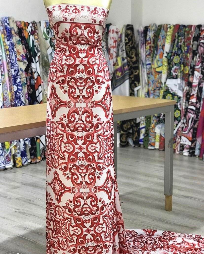 Red majolica pattern fabric with intricate floral design displayed on a mannequin in a fabric store.