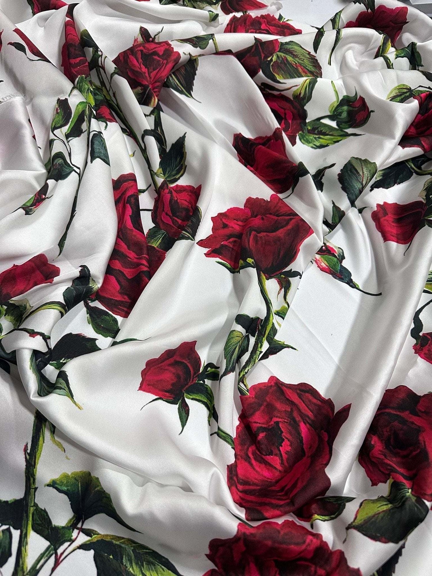White fabric with vibrant red rose pattern and green leaves, soft and smooth textile for sewing projects