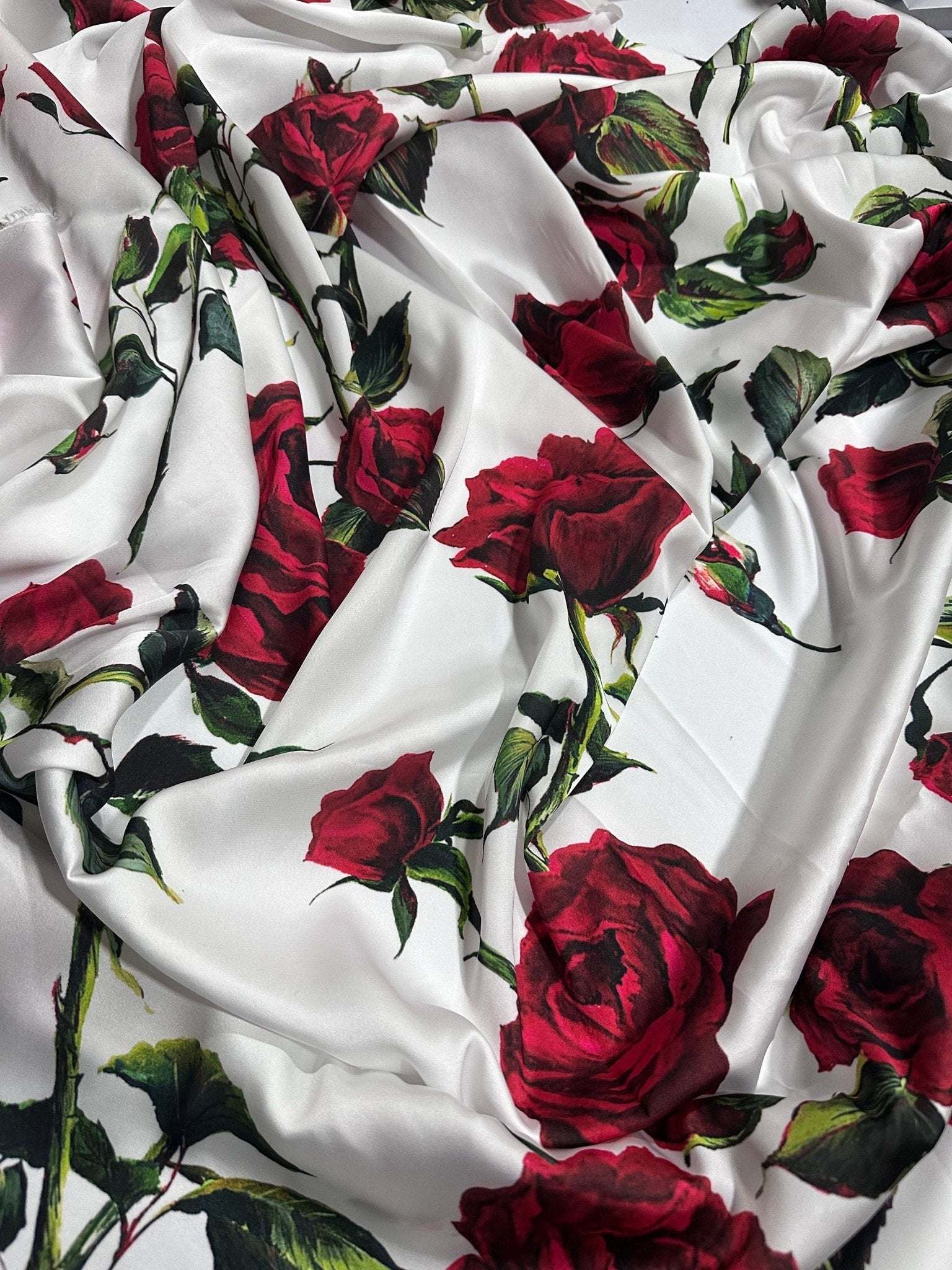 White fabric with vibrant red rose pattern and green leaves, soft and smooth textile for sewing projects