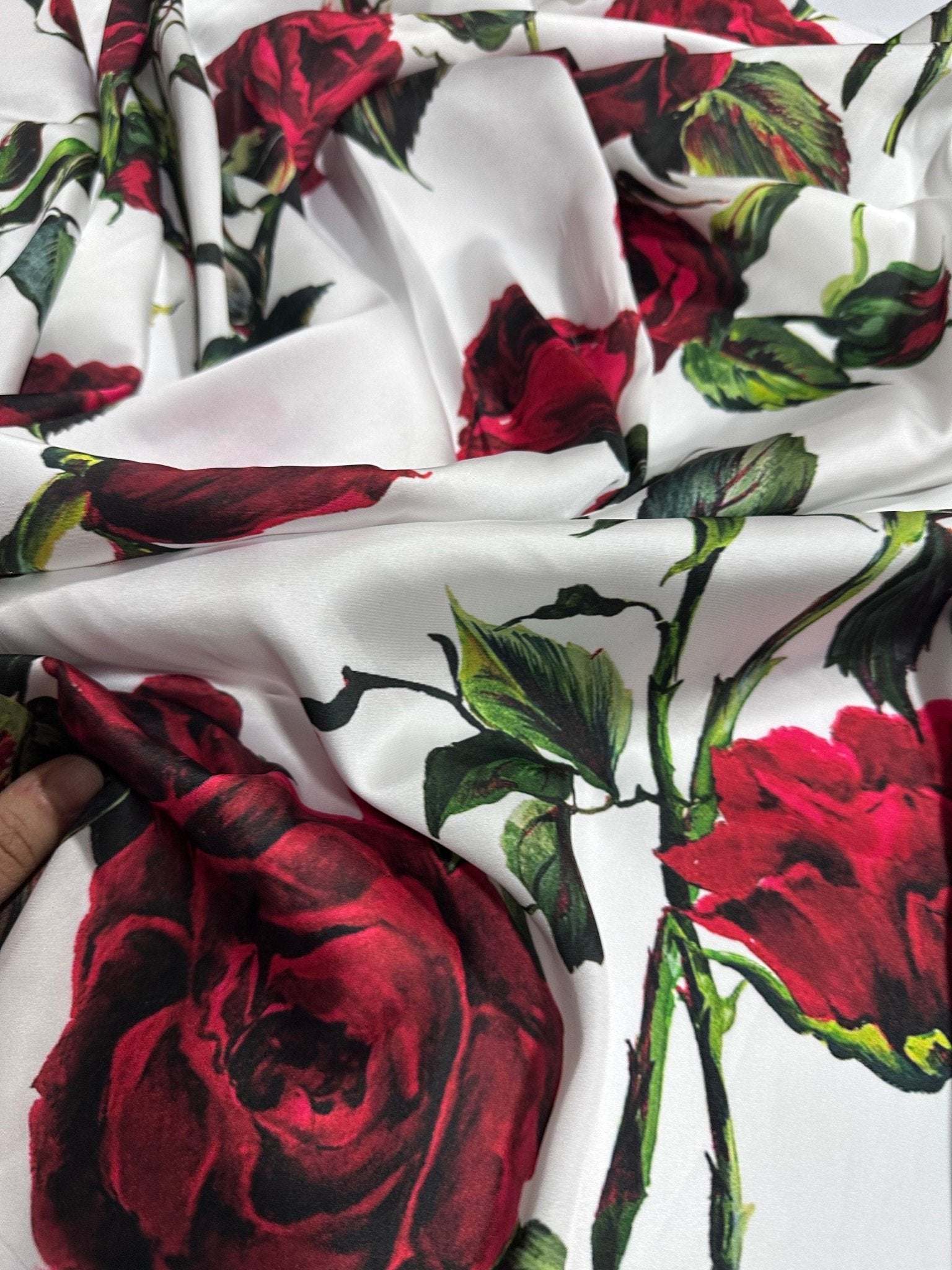 White fabric with vibrant red rose pattern and green leaves, smooth texture, suitable for sewing projects.