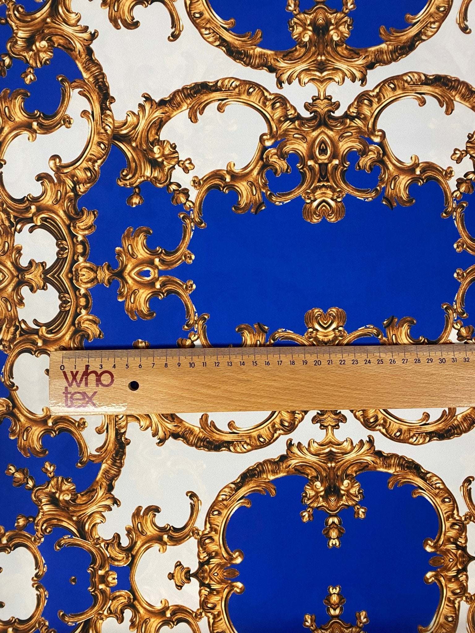 Royal blue fabric with intricate golden baroque pattern and measuring ruler for scale