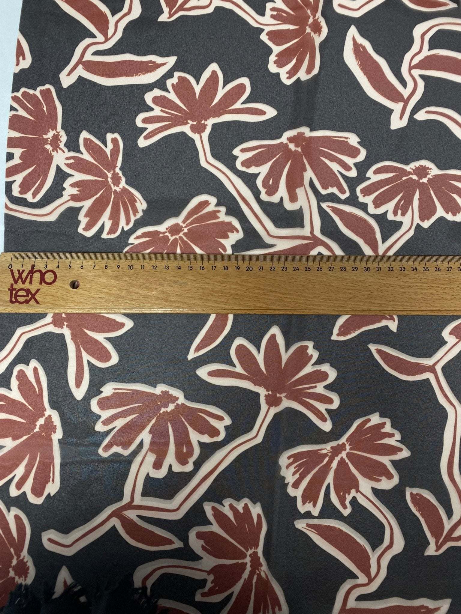 rust red floral print fabric with large flowers on black background with measuring ruler for scale