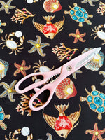 Black fabric with colorful sea shell, starfish, crab, turtle, and coral pattern with pink scissors on top