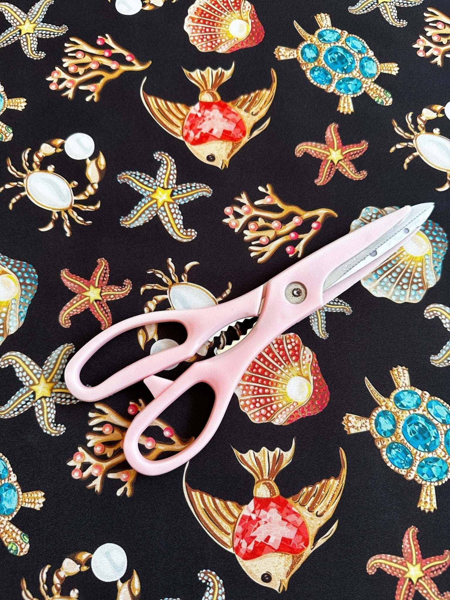 Black fabric with colorful sea shell, starfish, crab, turtle, and coral pattern with pink scissors on top