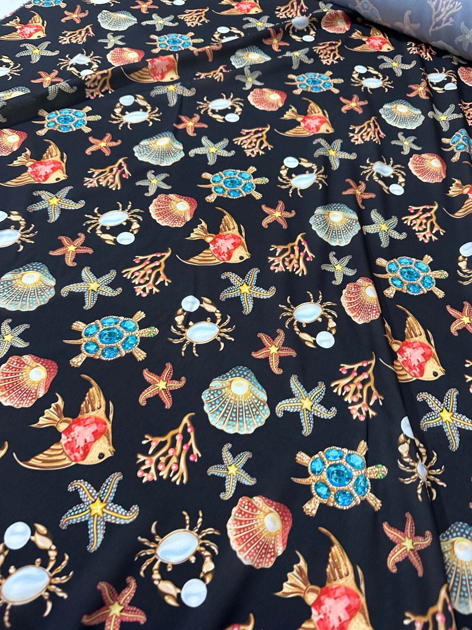 Sea shell and starfish pattern fabric with vibrant coastal-themed design on dark background, featuring turtles, crabs, and coral motifs.