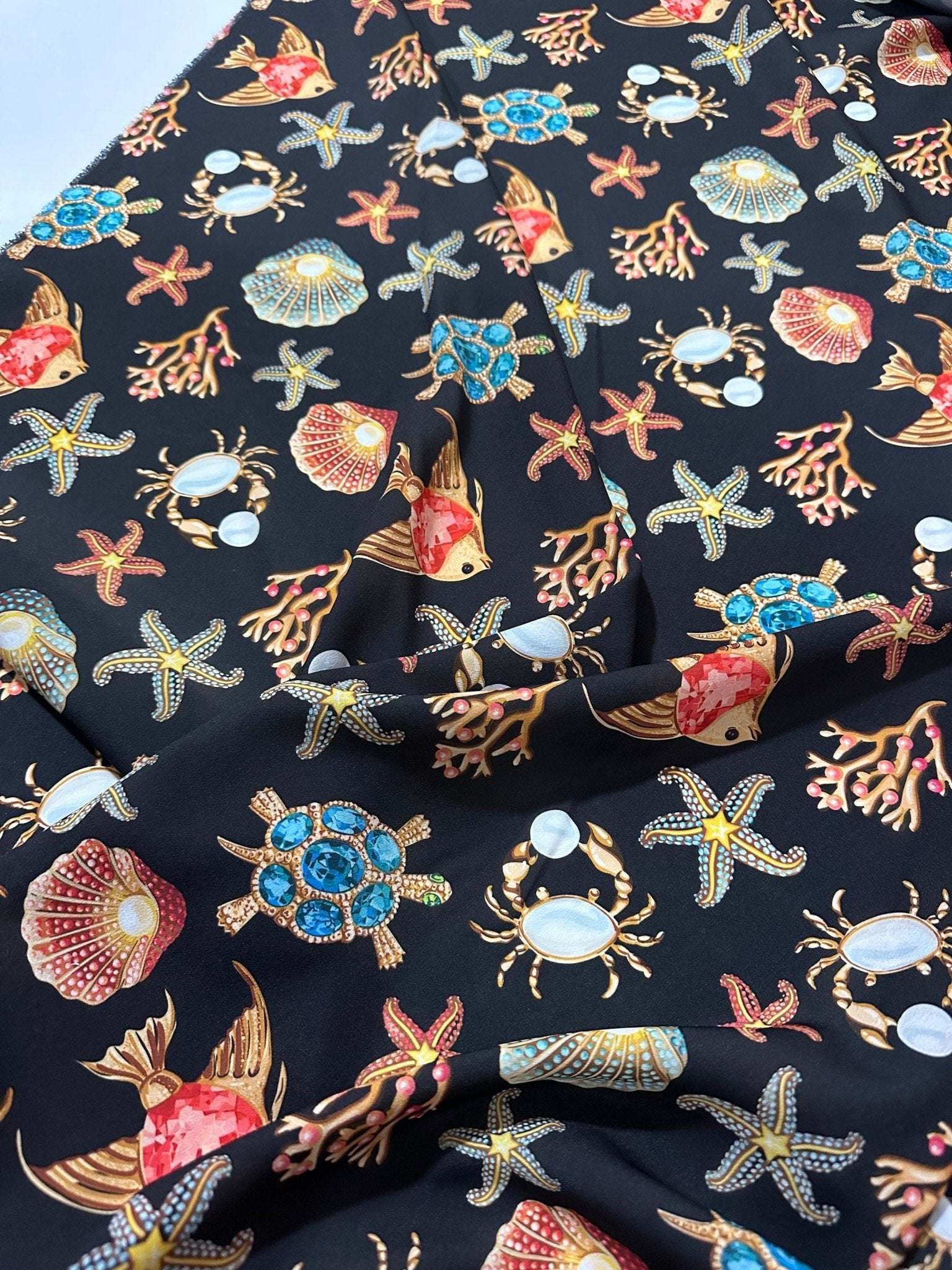 Black fabric with colorful sea shell, starfish, crab, and coral pattern design