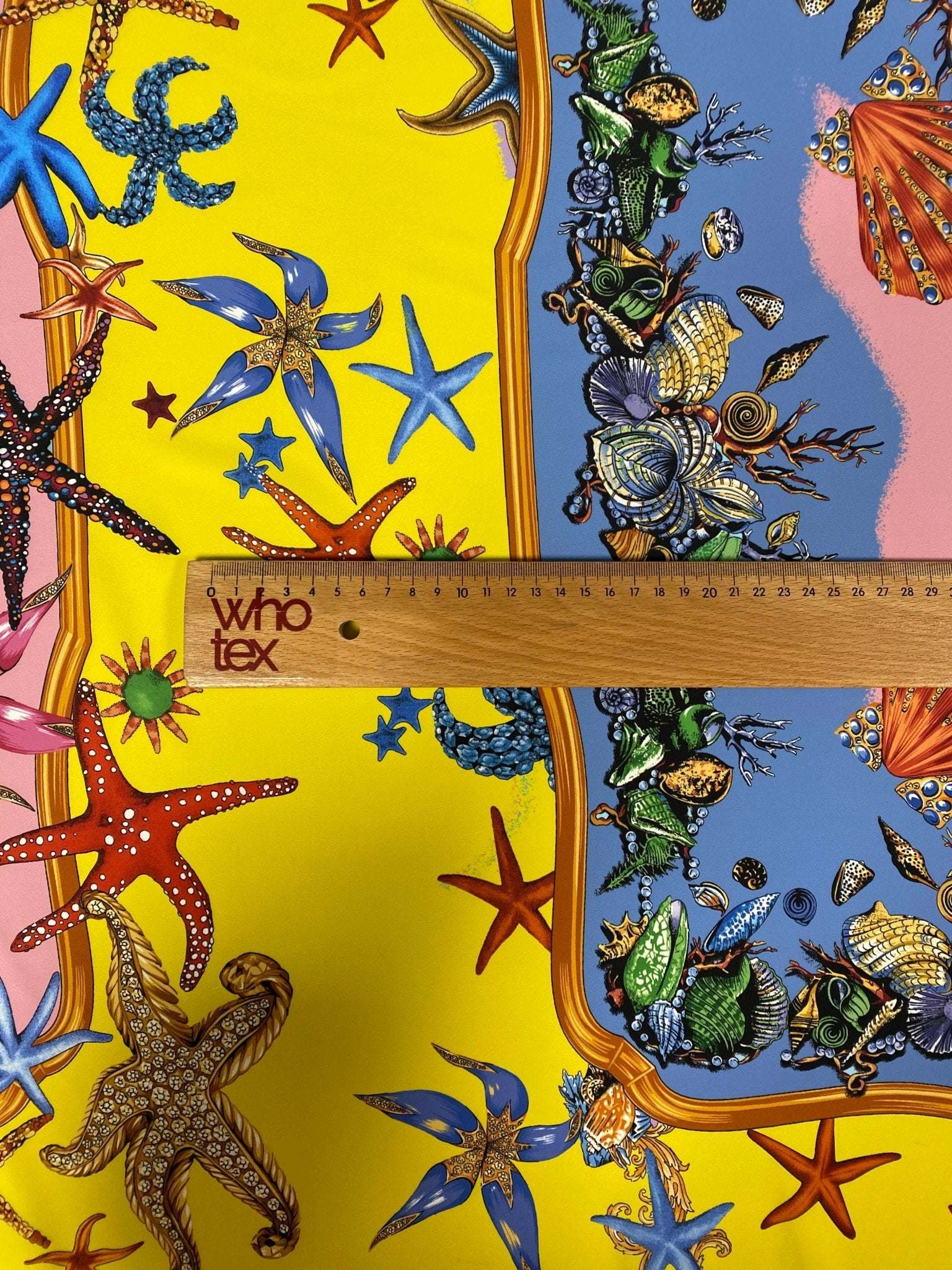 Close-up of colorful sea shells and starfish patterned fabric with a measuring ruler on yellow and blue background, Sea Shells Starfish Fabric design.