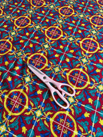 close-up of Sicilian pattern Bordeaux fabric with vibrant red, blue, yellow ornamental design and scissors on top