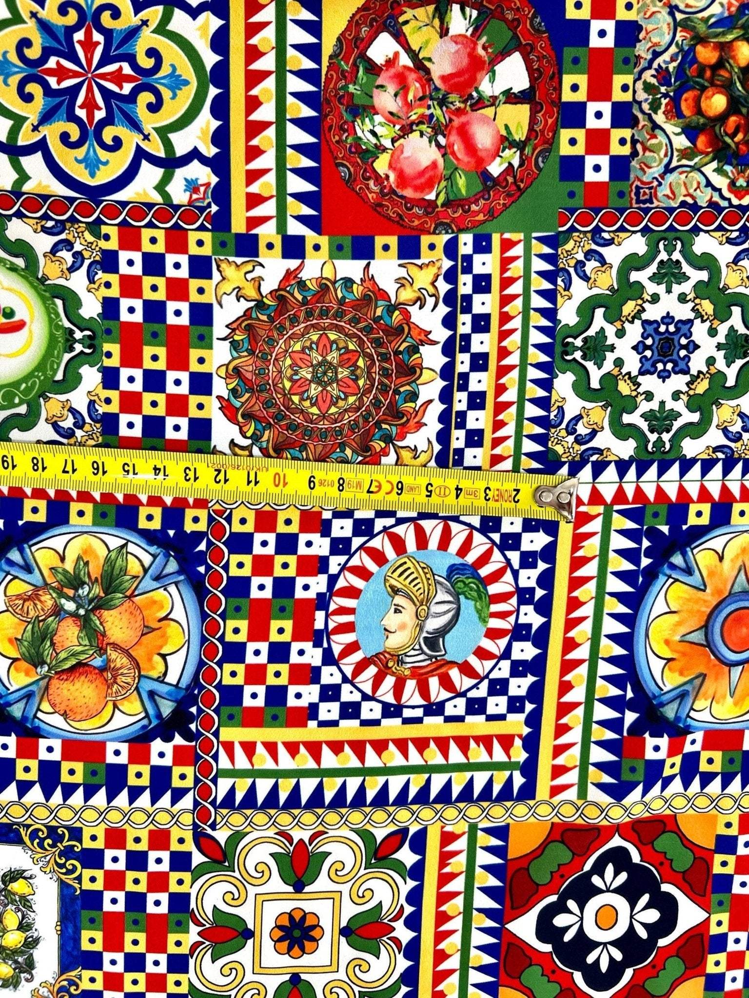 colorful Sicilian pattern Italian fabric with intricate geometric and floral designs in vibrant red, blue, yellow, and green colors, featuring traditional Sicilian motifs and a measuring tape across the fabric