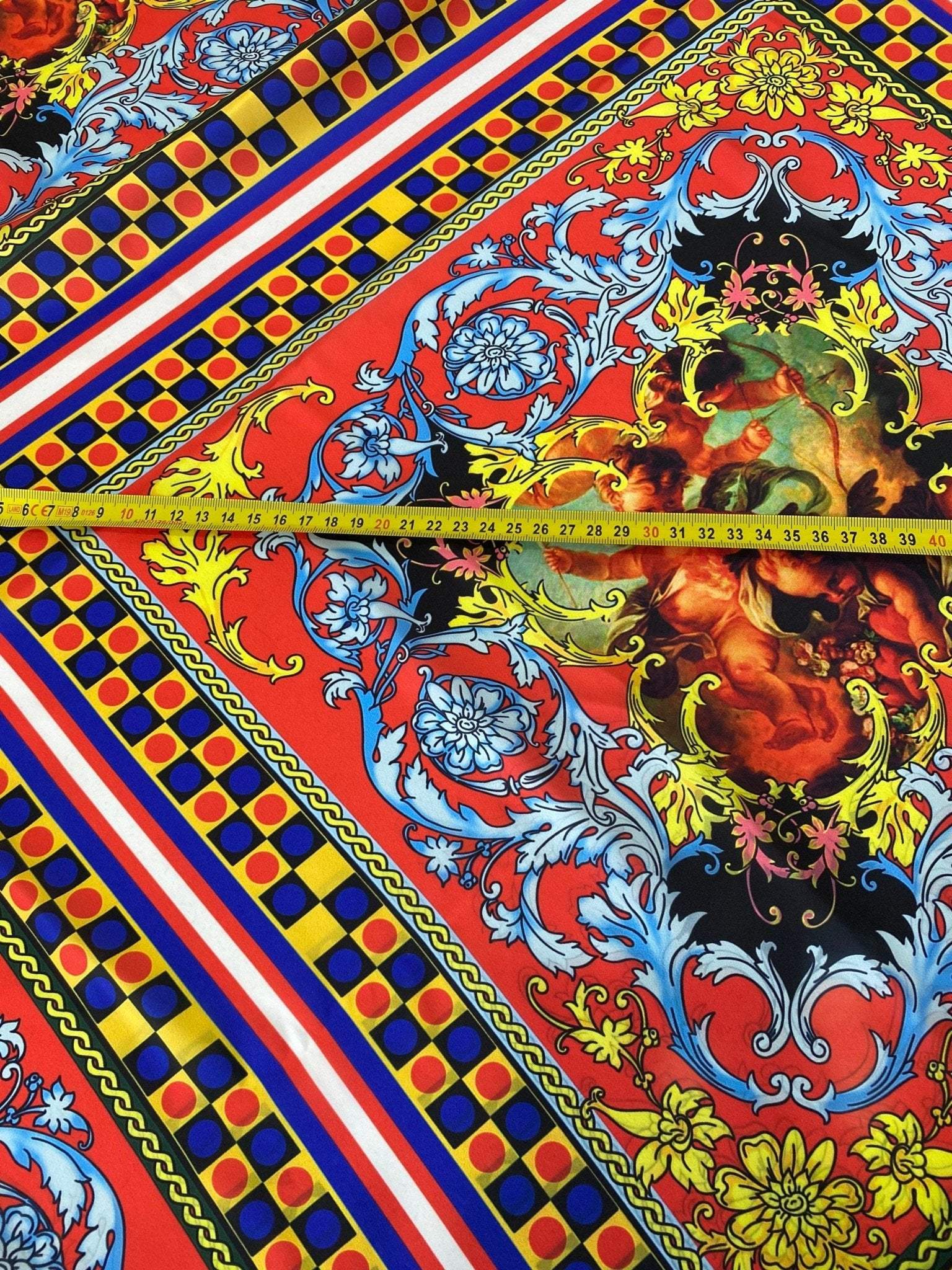 Close-up of vibrant red and blue Sicilian pattern fabric with intricate floral and geometric designs and a measuring tape showing width
