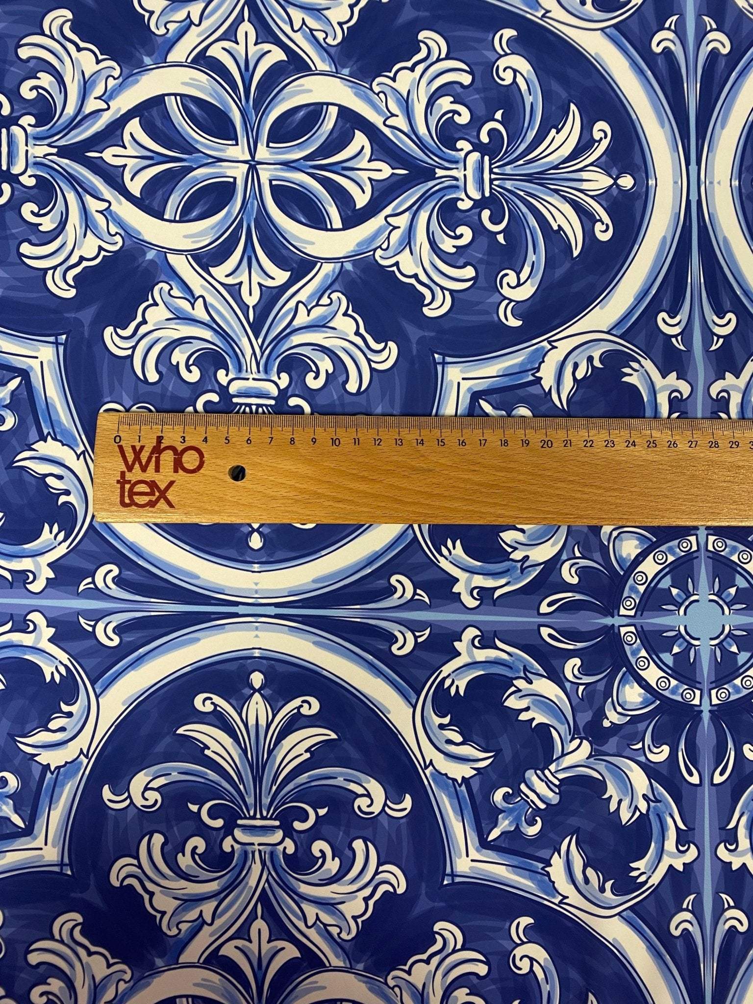 Close-up of blue and white Sicilian print fabric with intricate floral and geometric patterns and a wooden ruler for scale