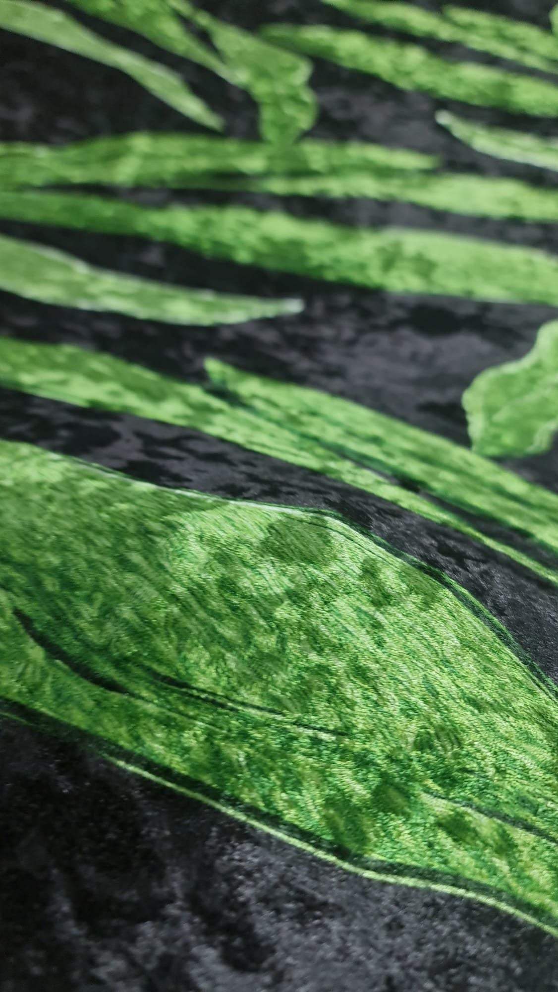 Close-up of silky velvet fabric with a green leaf pattern on black background, showcasing smooth texture and elegant drape.