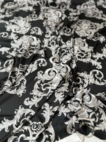 Close-up of silver baroque patterned fabric on black background with textured folds and rich design