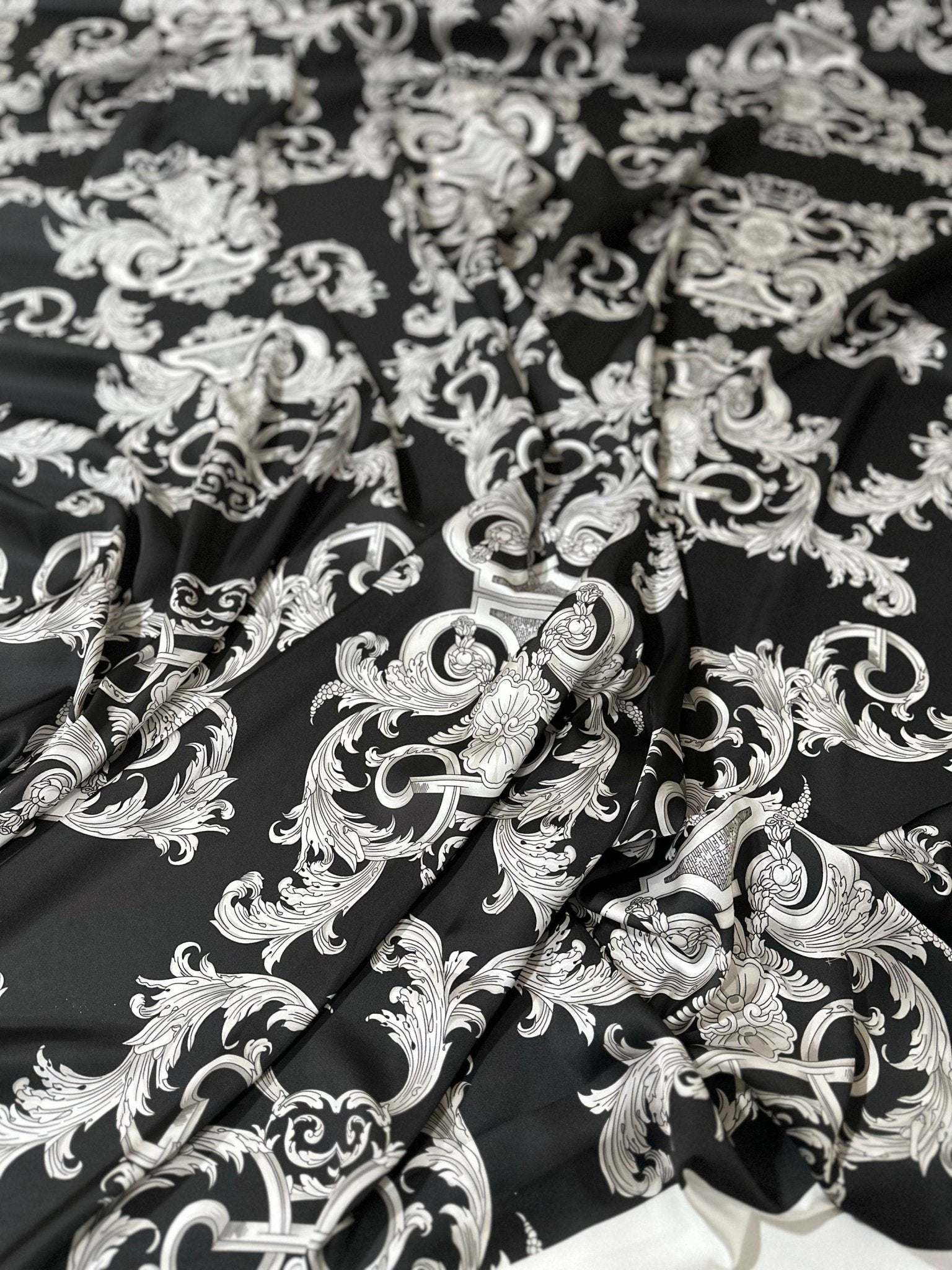 Close-up of silver baroque patterned fabric on black background with textured folds and rich design