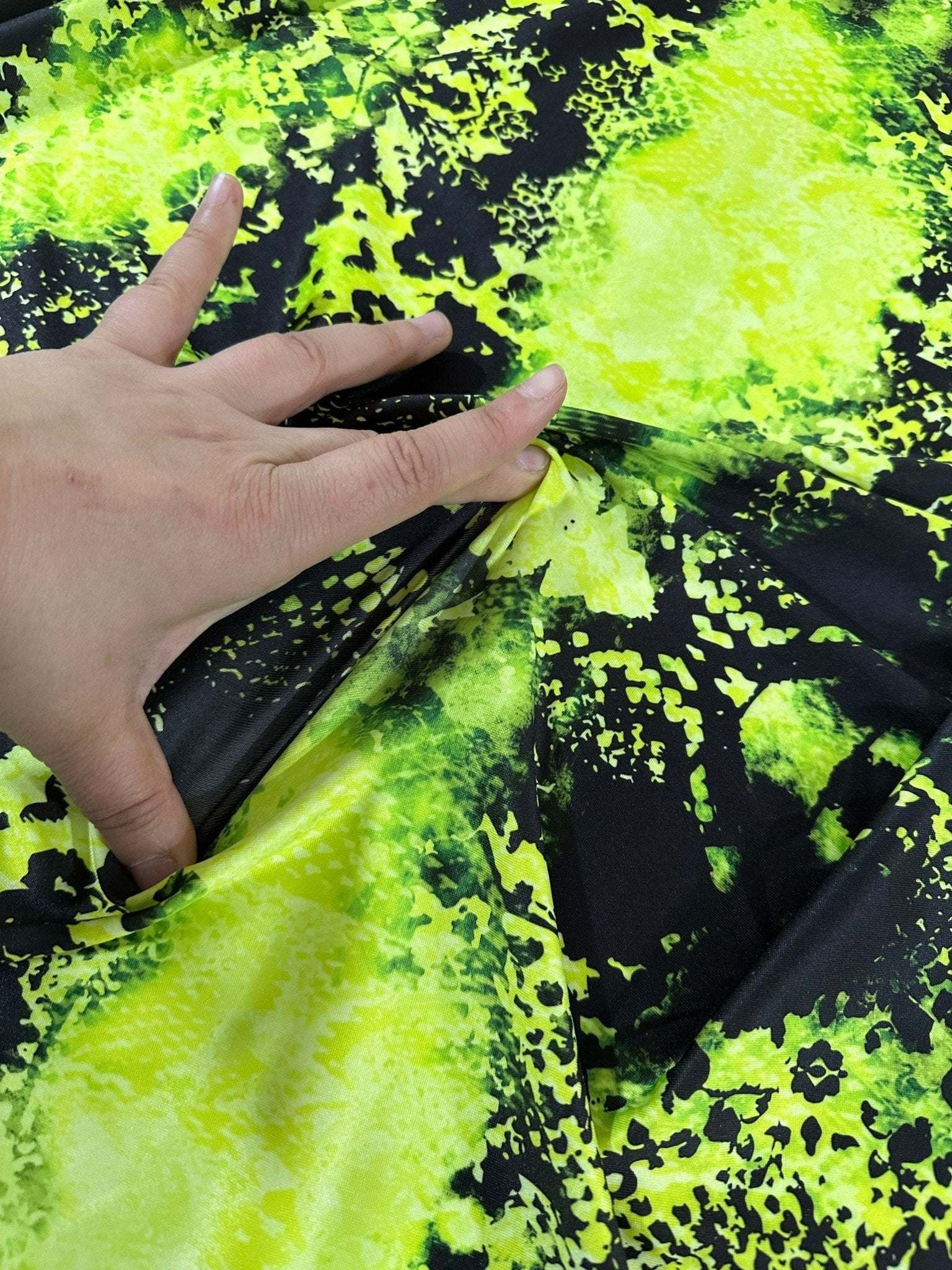 Close-up of neon green spandex fabric with black pattern being stretched by hand