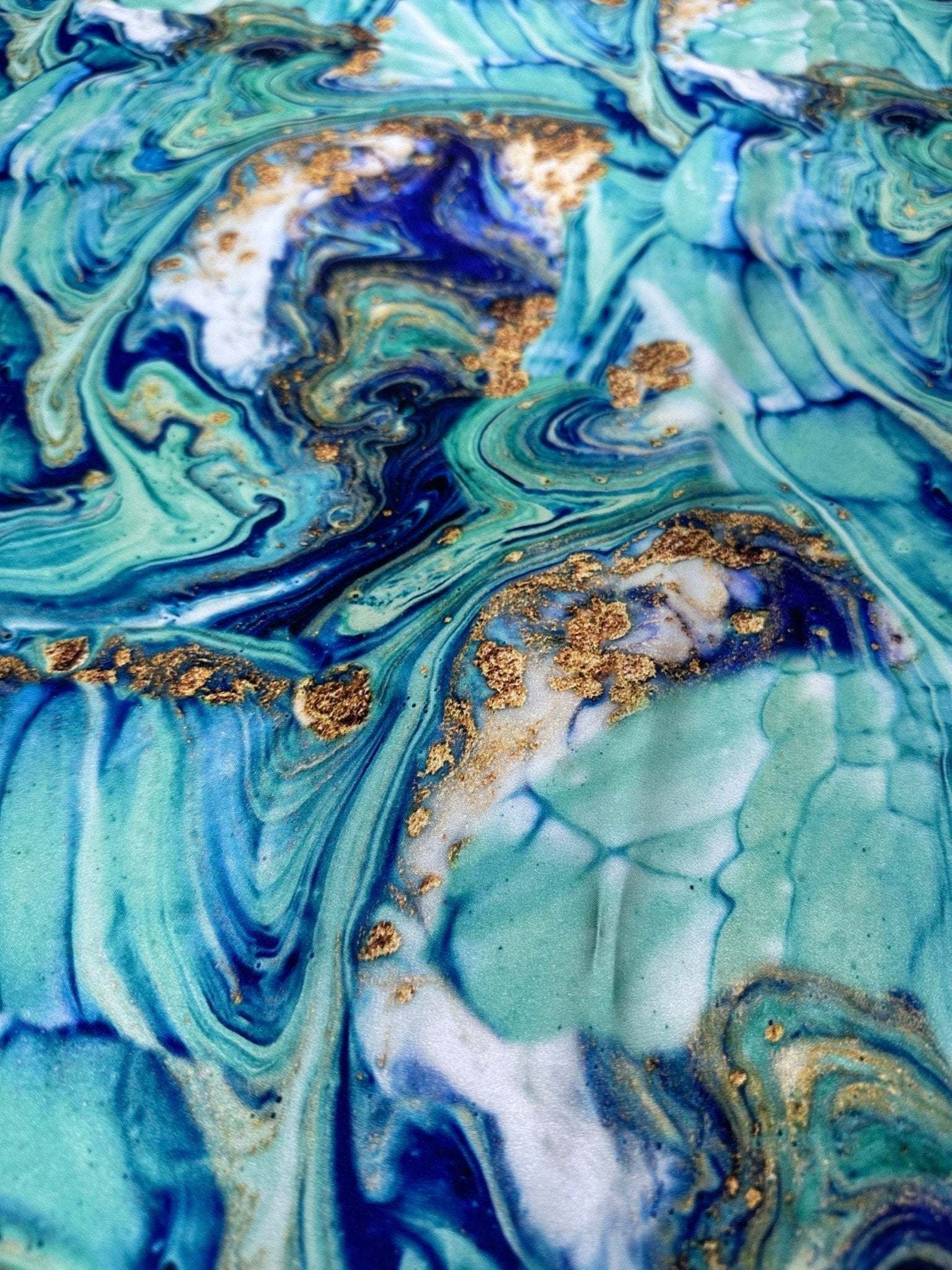 Close-up of turquoise and blue marble print fabric with gold accents and swirling patterns