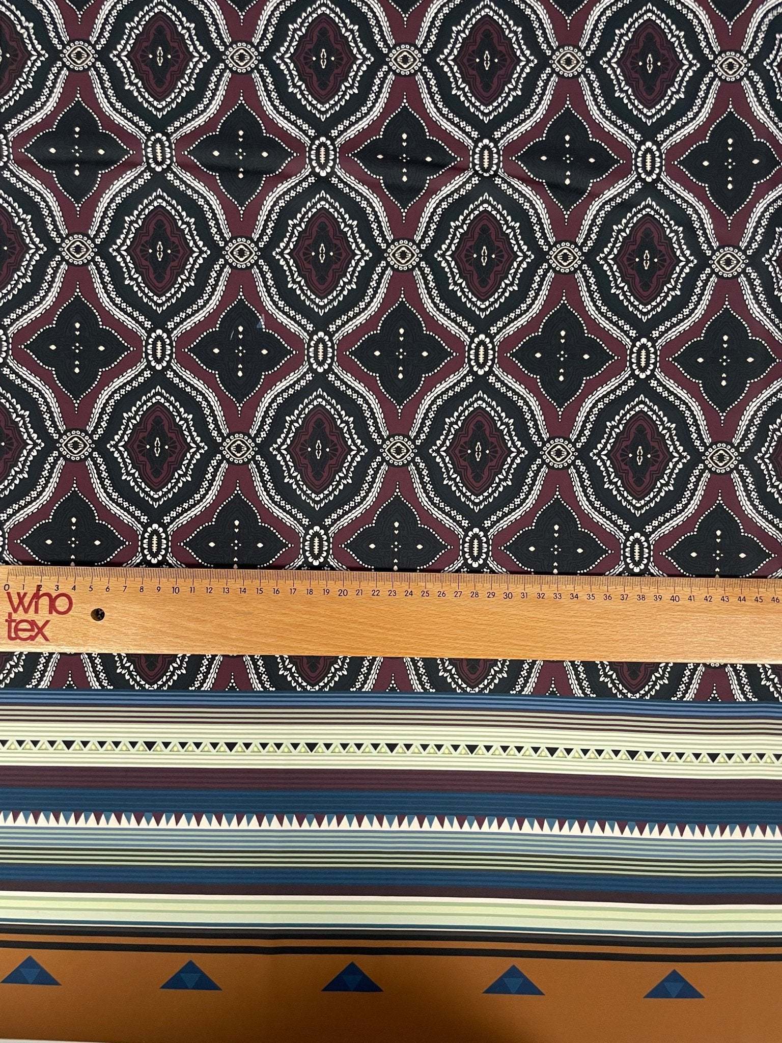 Burgundy and black geometric patterned fabric with ethnic striped edge and measuring ruler for scale