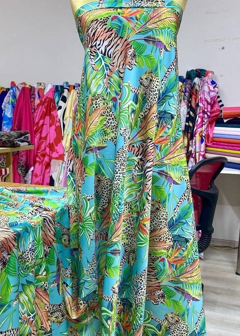 Fabric bundle with tropical leaves and leopard patterns in vibrant colors on a turquoise background displayed on a dress form in a fabric store.