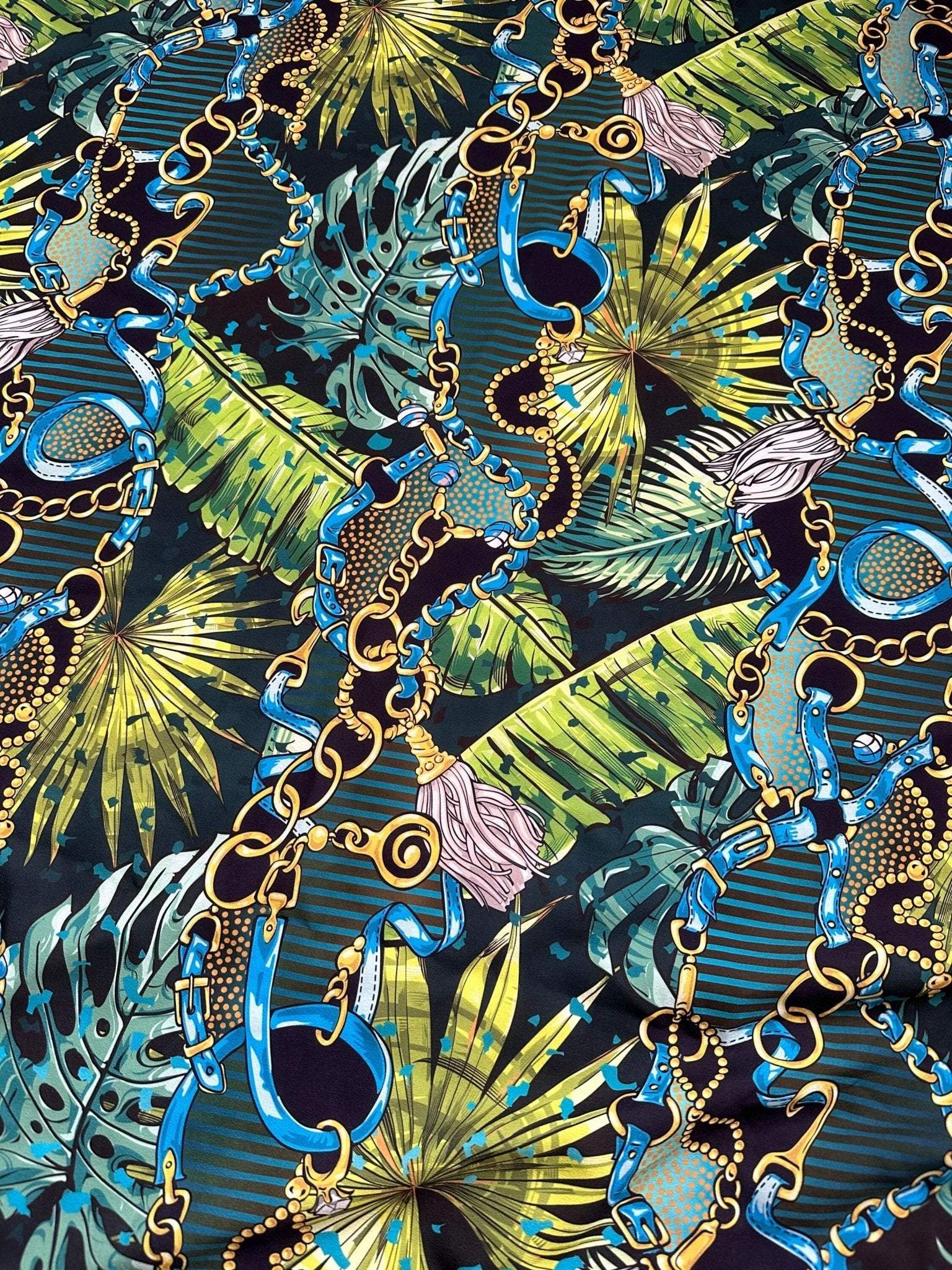 Tropical fabric with vibrant chain belt pattern featuring blue and gold chains over green tropical leaves design