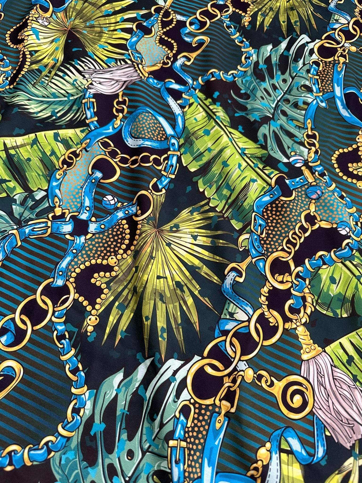 Tropical fabric with vibrant chain belt pattern featuring blue, gold chains and green tropical leaves on dark background