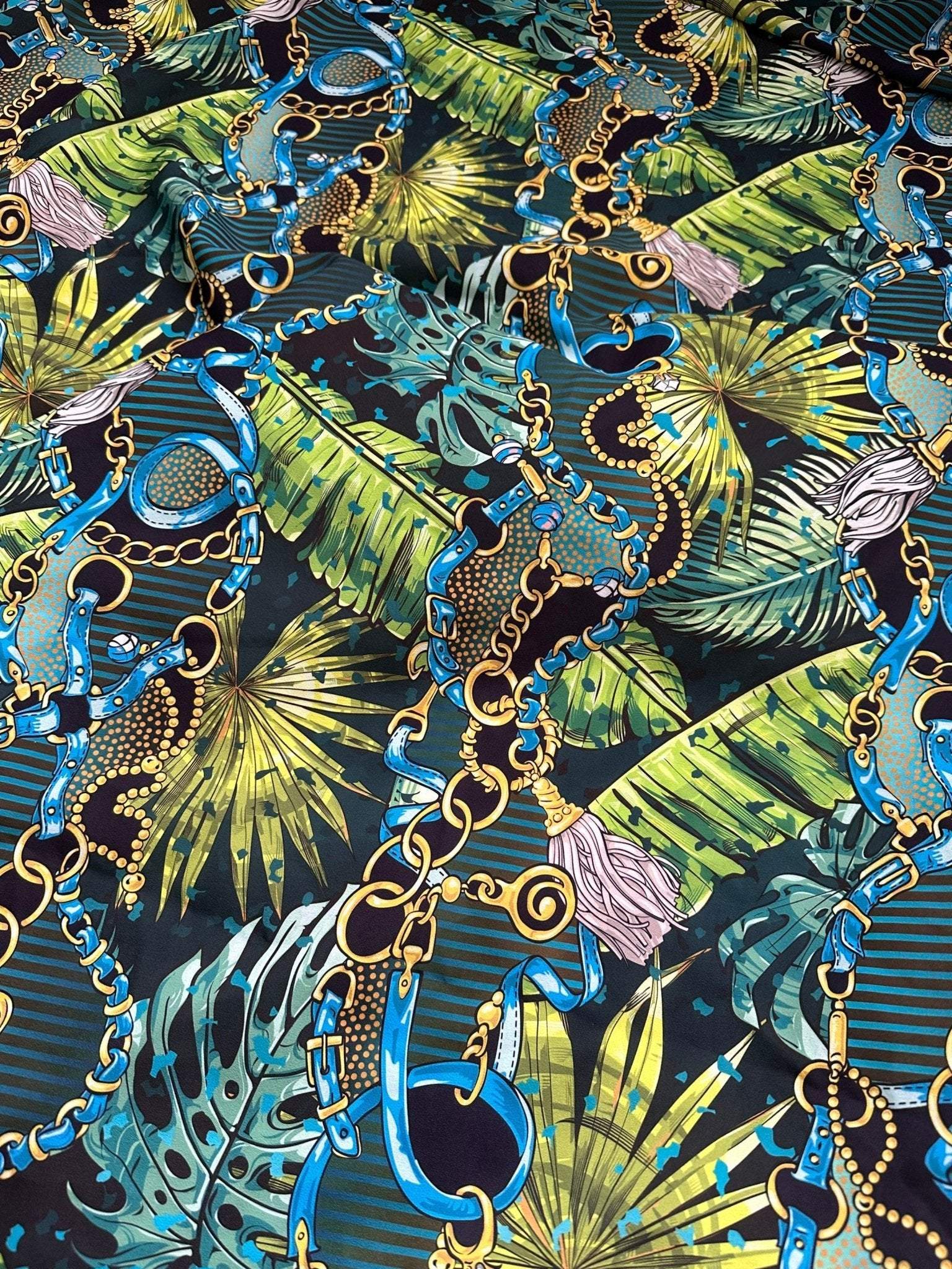 Tropical fabric with vibrant chain belt pattern featuring blue chains, gold details, and green tropical leaves on dark background