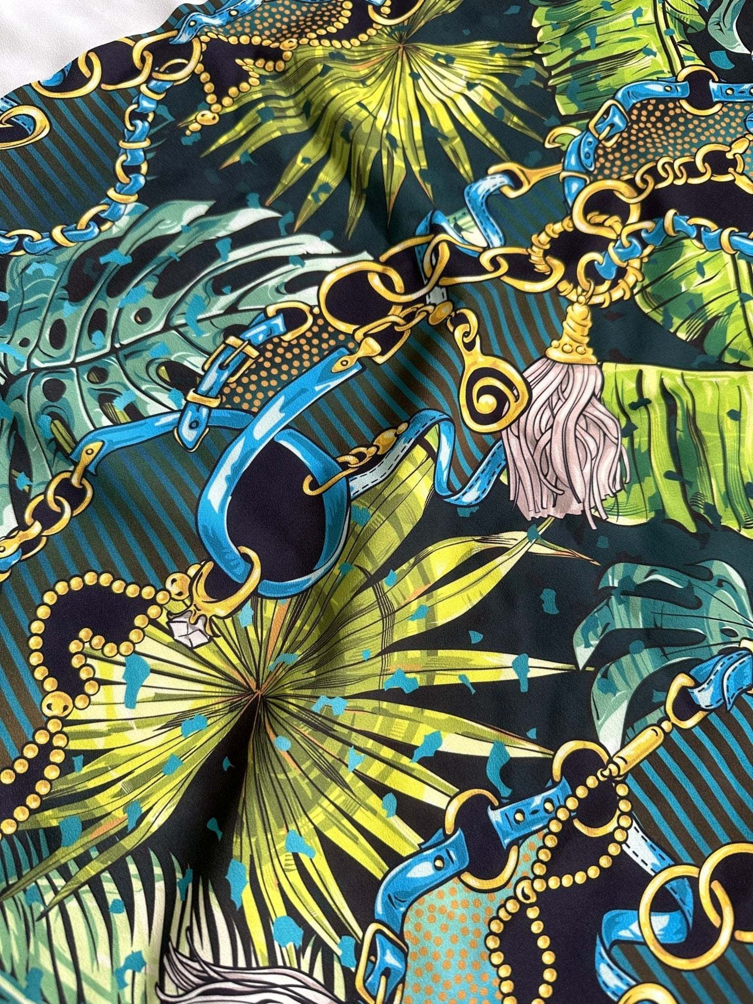 Tropical fabric with vibrant chain belt pattern featuring blue belts, gold chains, and green tropical leaves on dark background