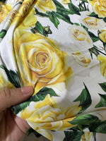 Close-up of yellow floral rose pattern fabric held in hand with green leaves on white background