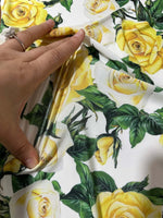 Close-up of yellow floral rose pattern fabric with green leaves and hand displaying fabric texture