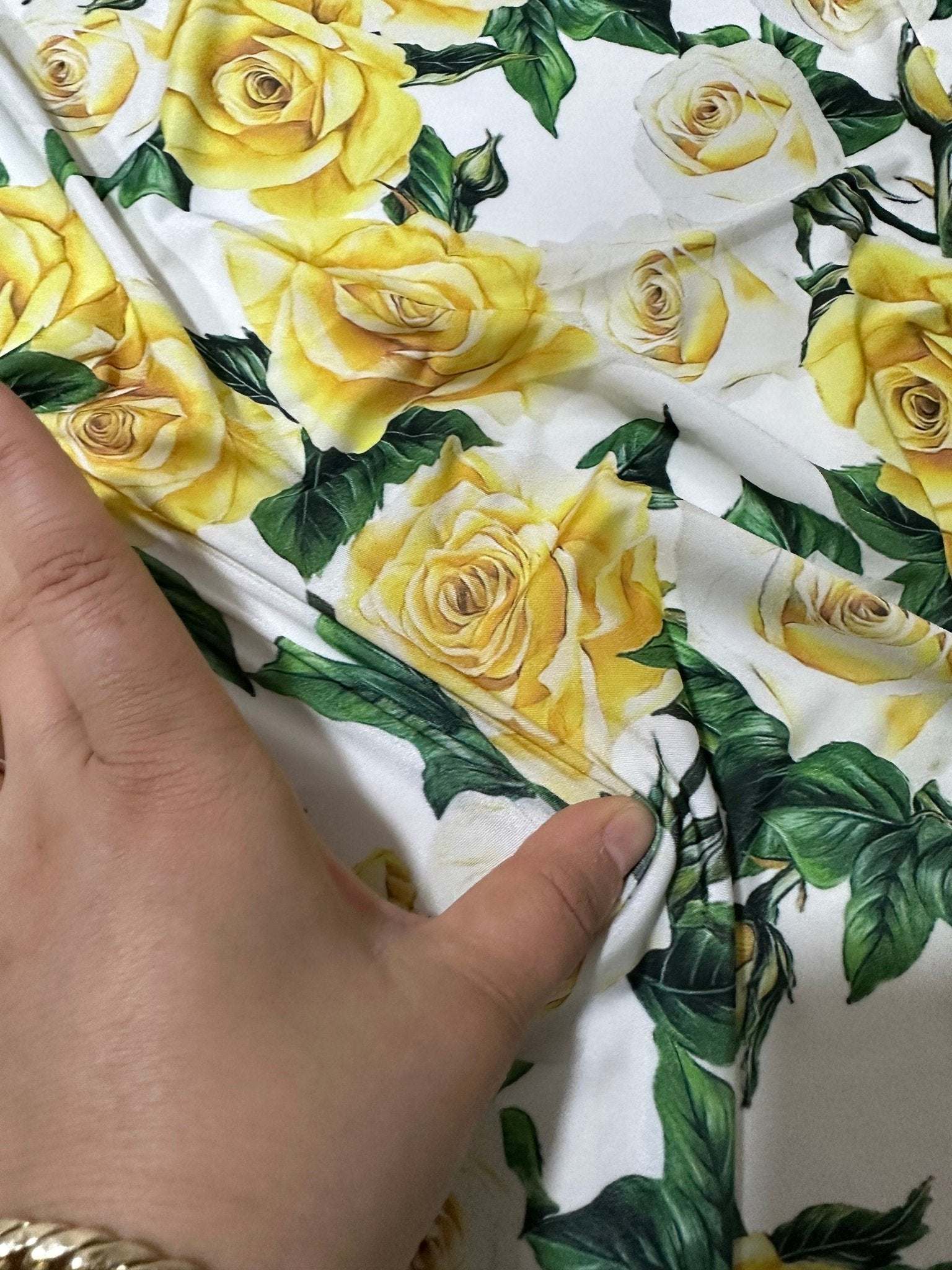 Close-up of yellow floral rose pattern fabric with green leaves being held and stretched by a hand