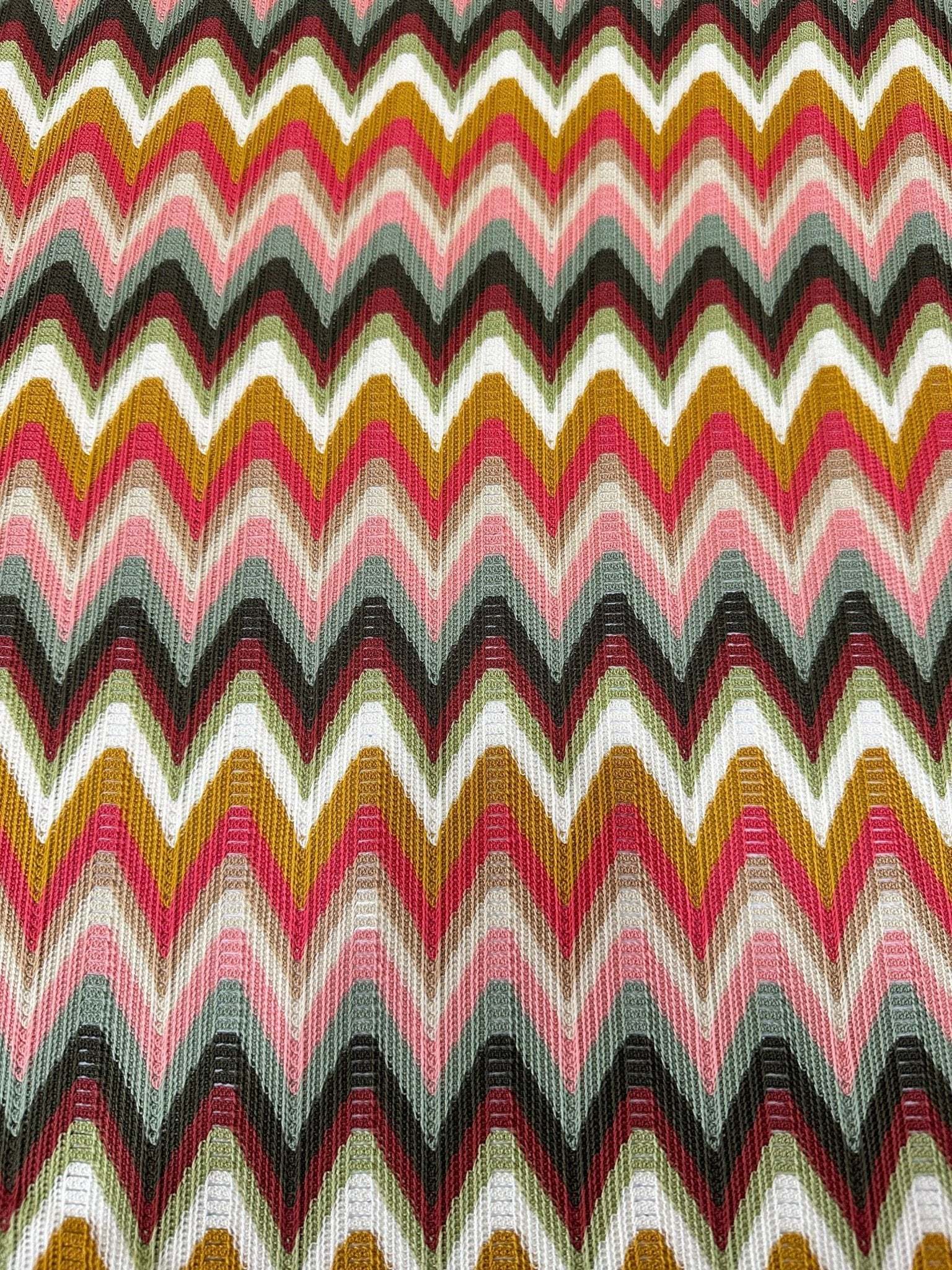 Luxury autumn chevron zigzag knit jersey fabric with warm tones of pink, mustard, black, and white, ideal for elegant autumn attire.