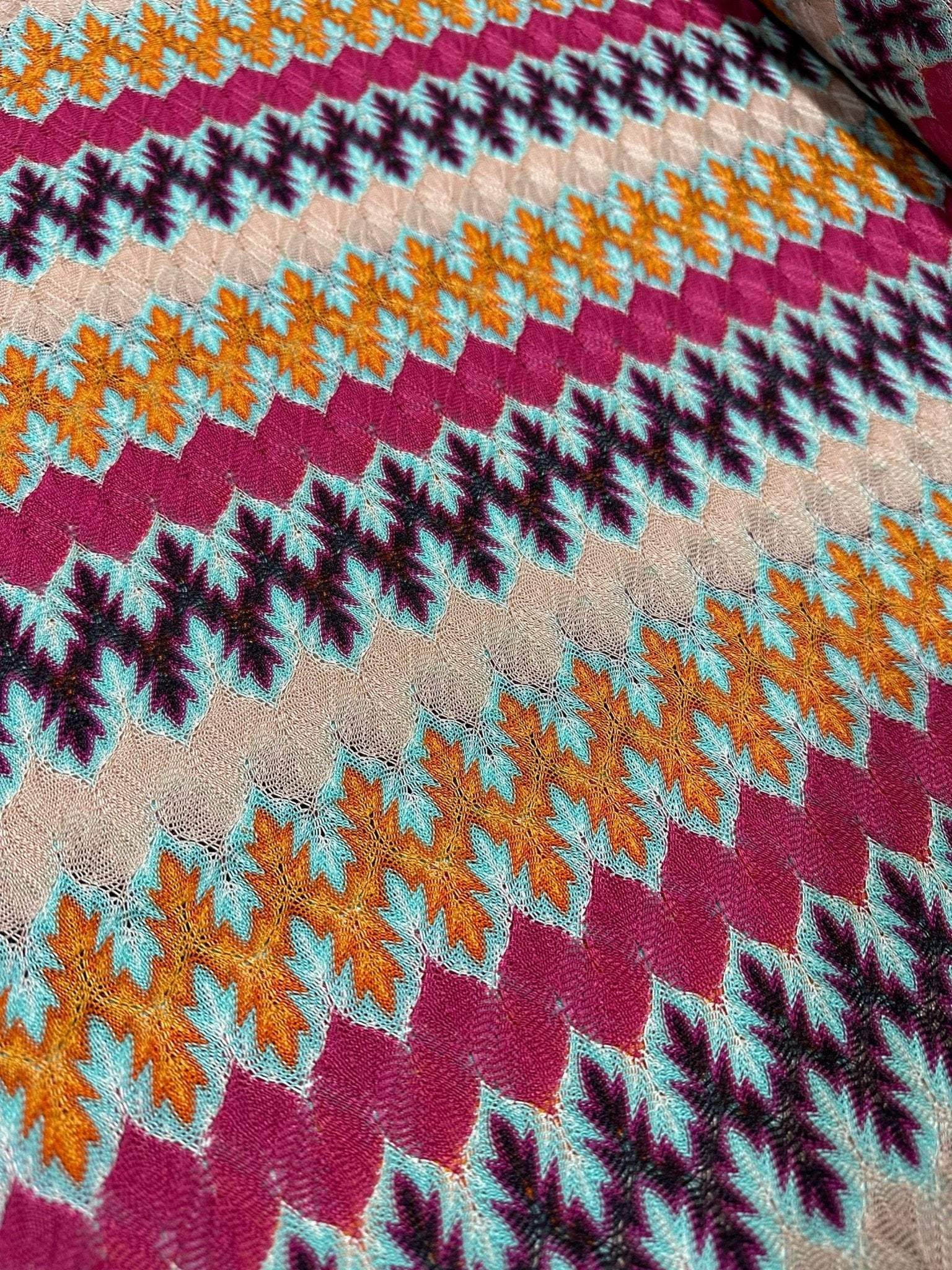 Close-up of multicolor zigzag knit jersey fabric with chevron pattern in orange, blue, beige, and burgundy tones.